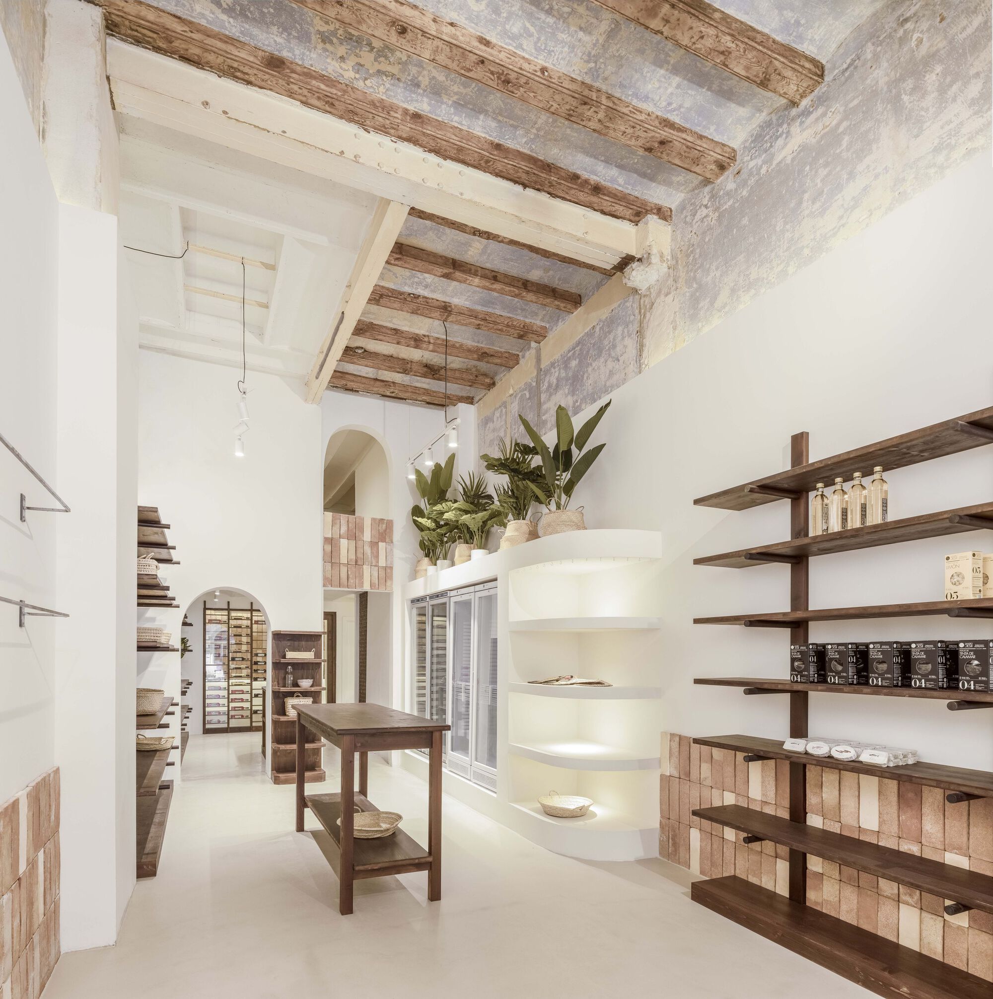 Interior retail space with exposed timber ceiling beams, white plaster walls and wooden shelving displaying products