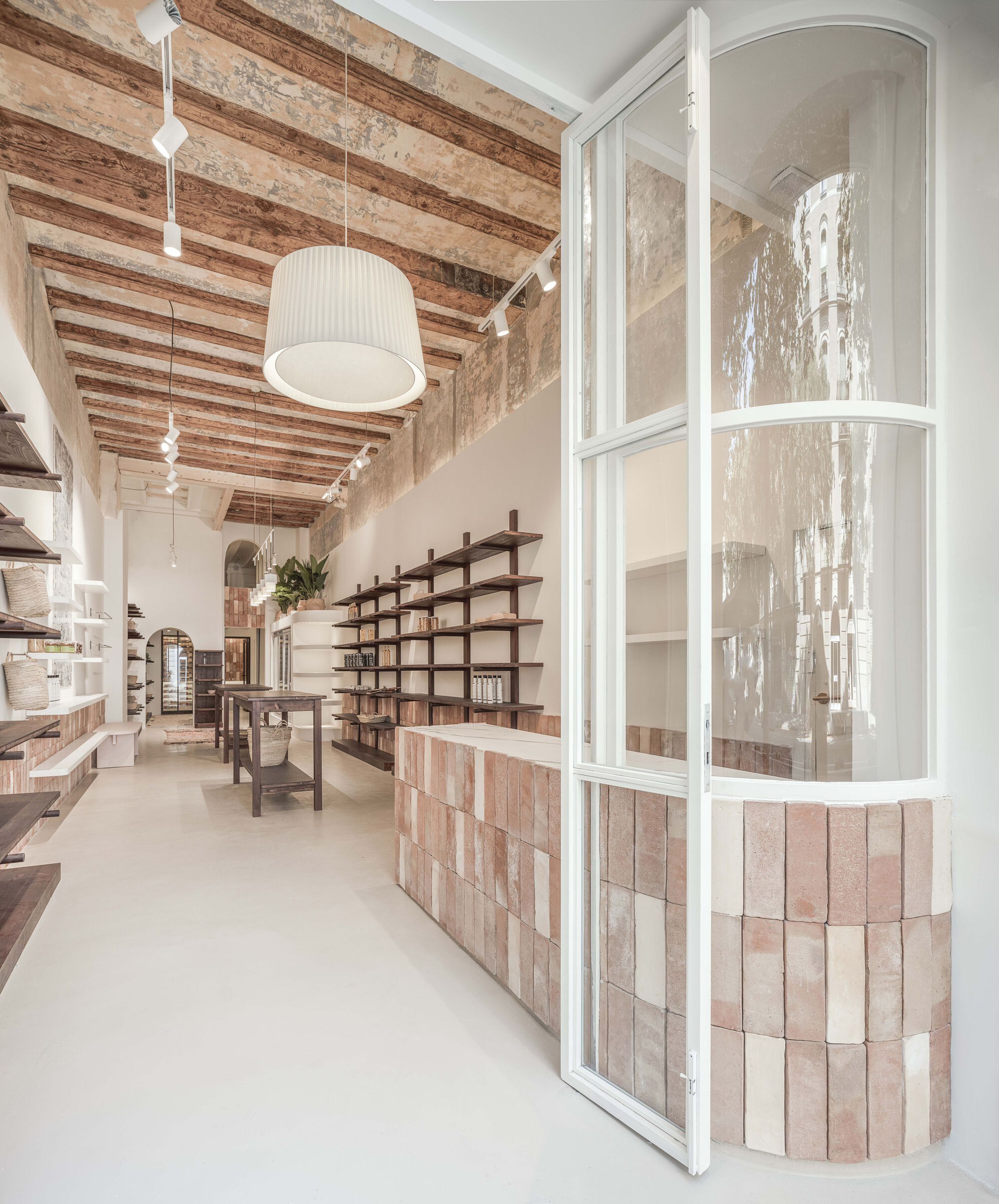 Long interior view showing curved glass partition with tiled base and dark timber shelving along the corridor