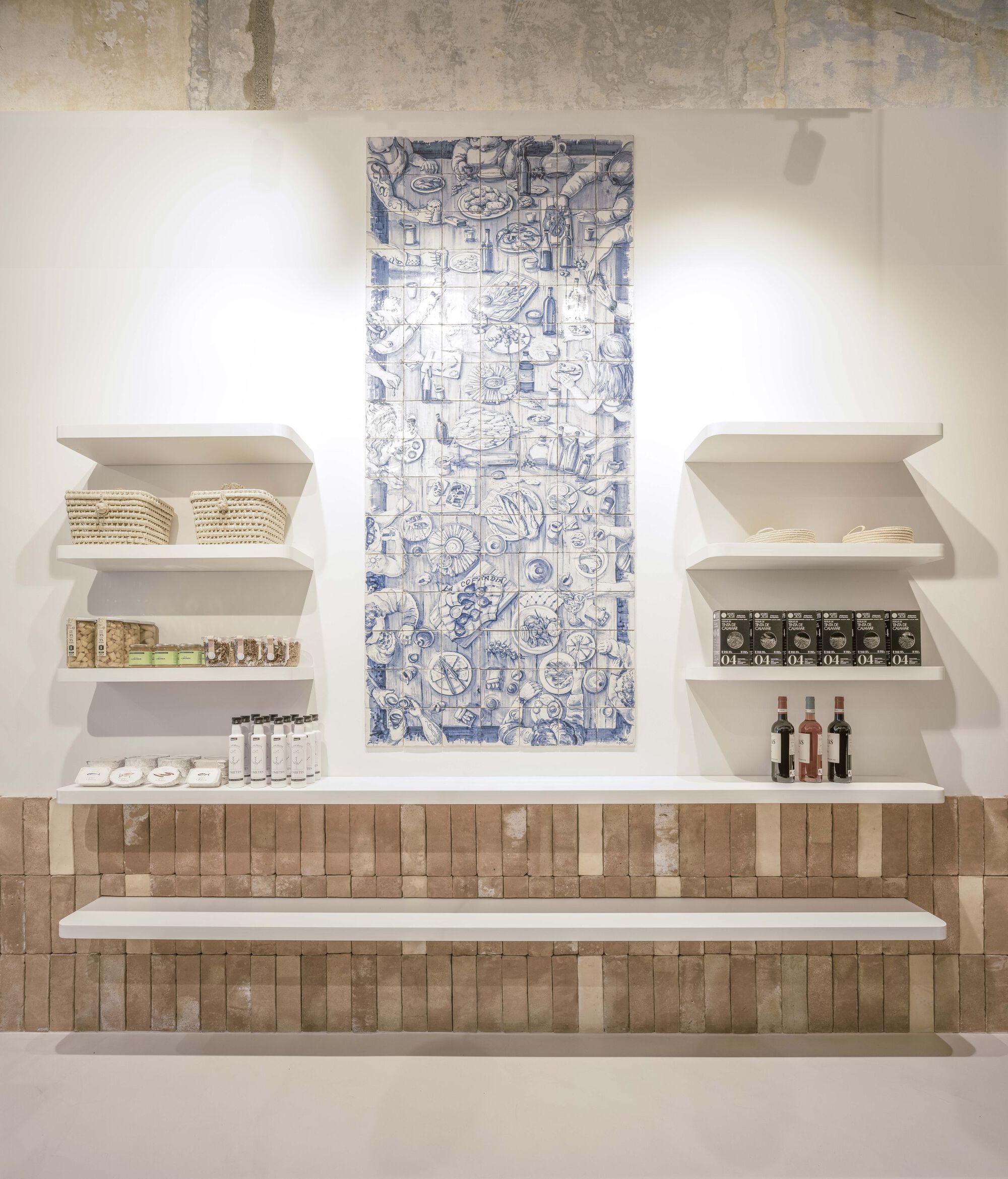 Display wall with blue and white ceramic tile panel above white shelves and terracotta brick base