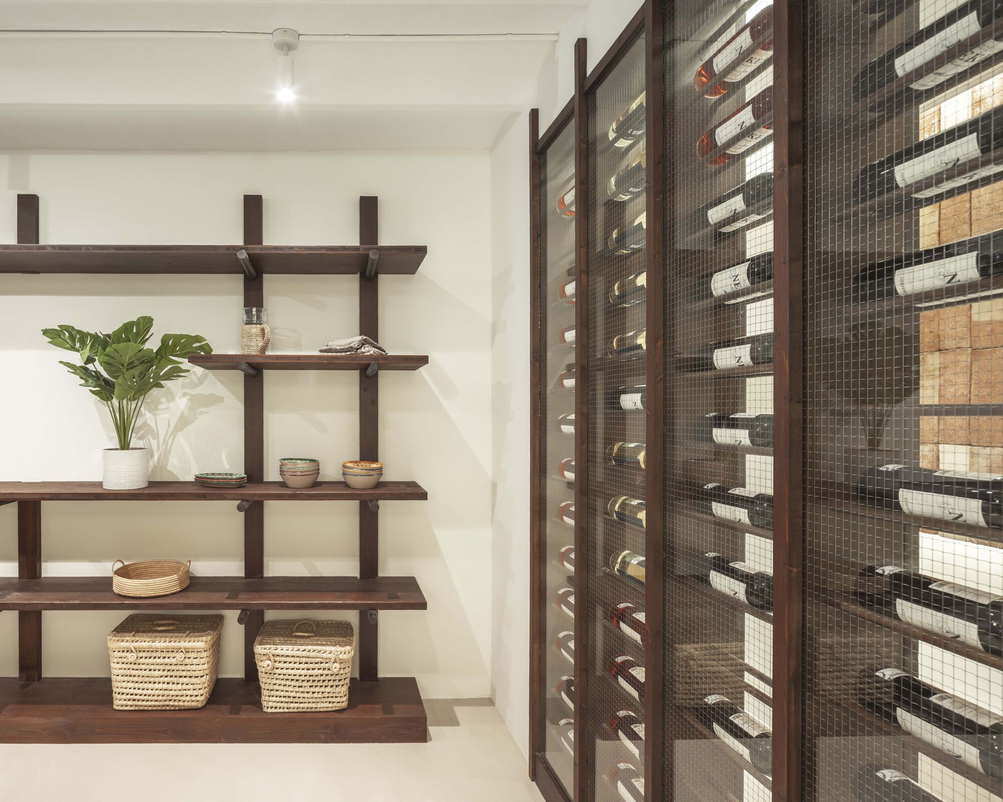 Wine storage alcove with dark timber and wire mesh rack beside open wooden shelving with potted plant