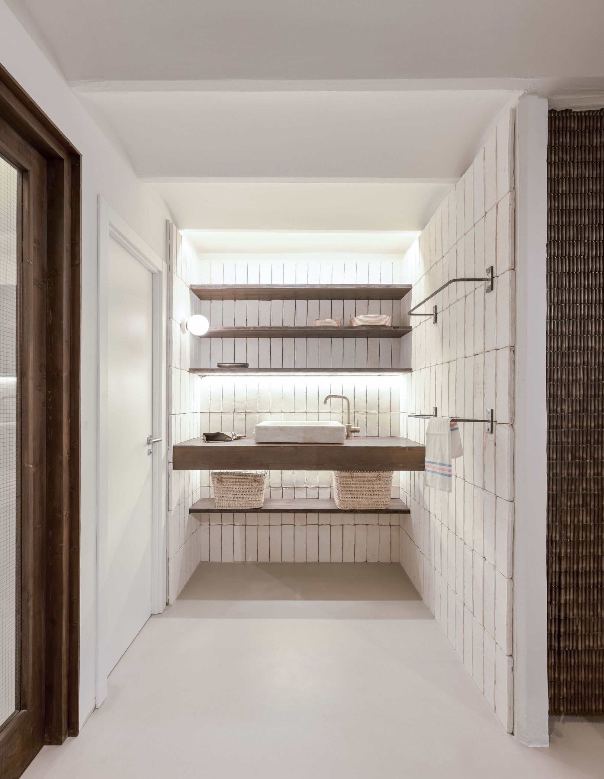 Bathroom with vertical white tile walls and timber floating shelves beneath a skylight