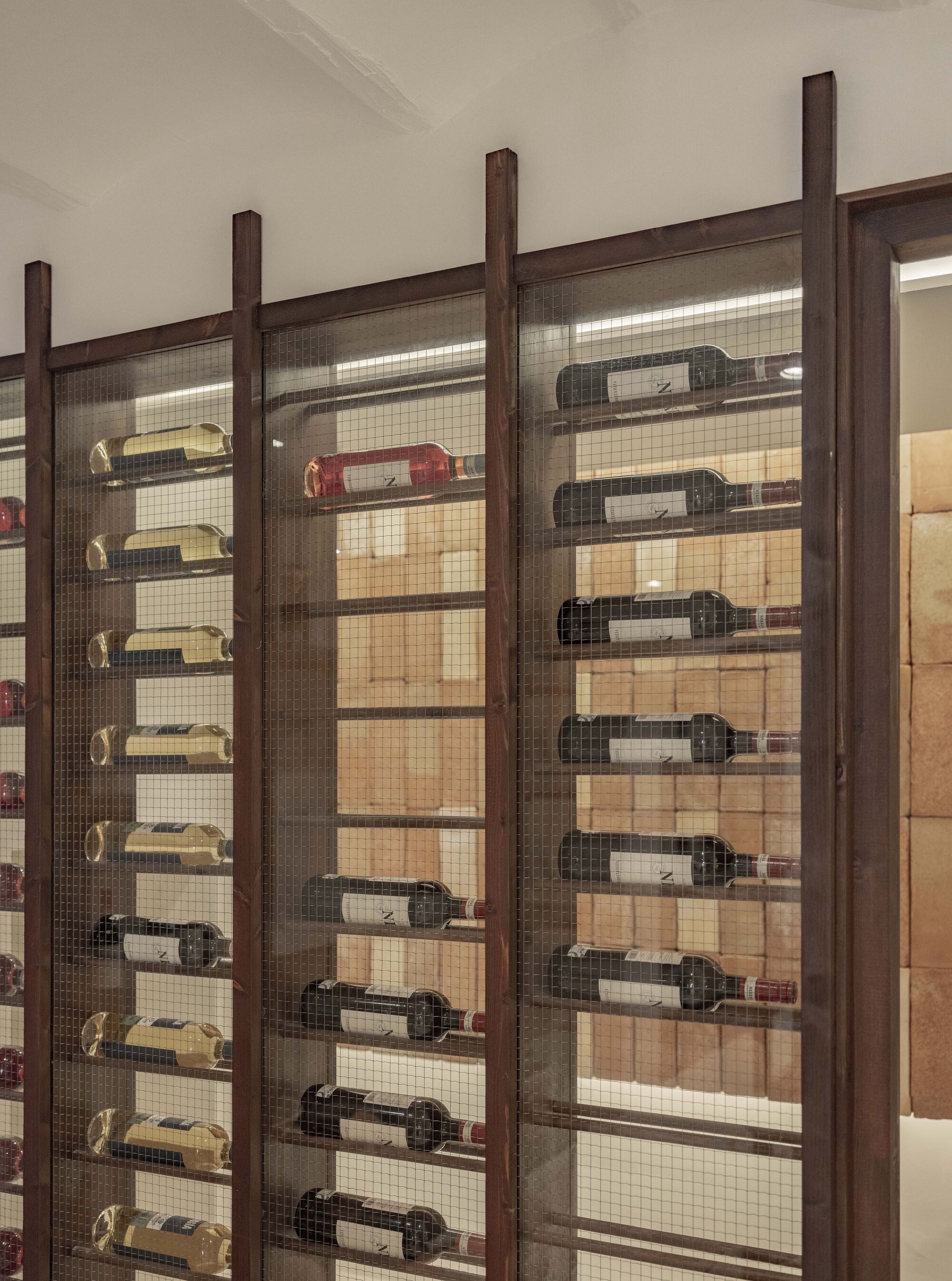 Close-up of wine bottles displayed horizontally on metal pegs within timber and mesh screen