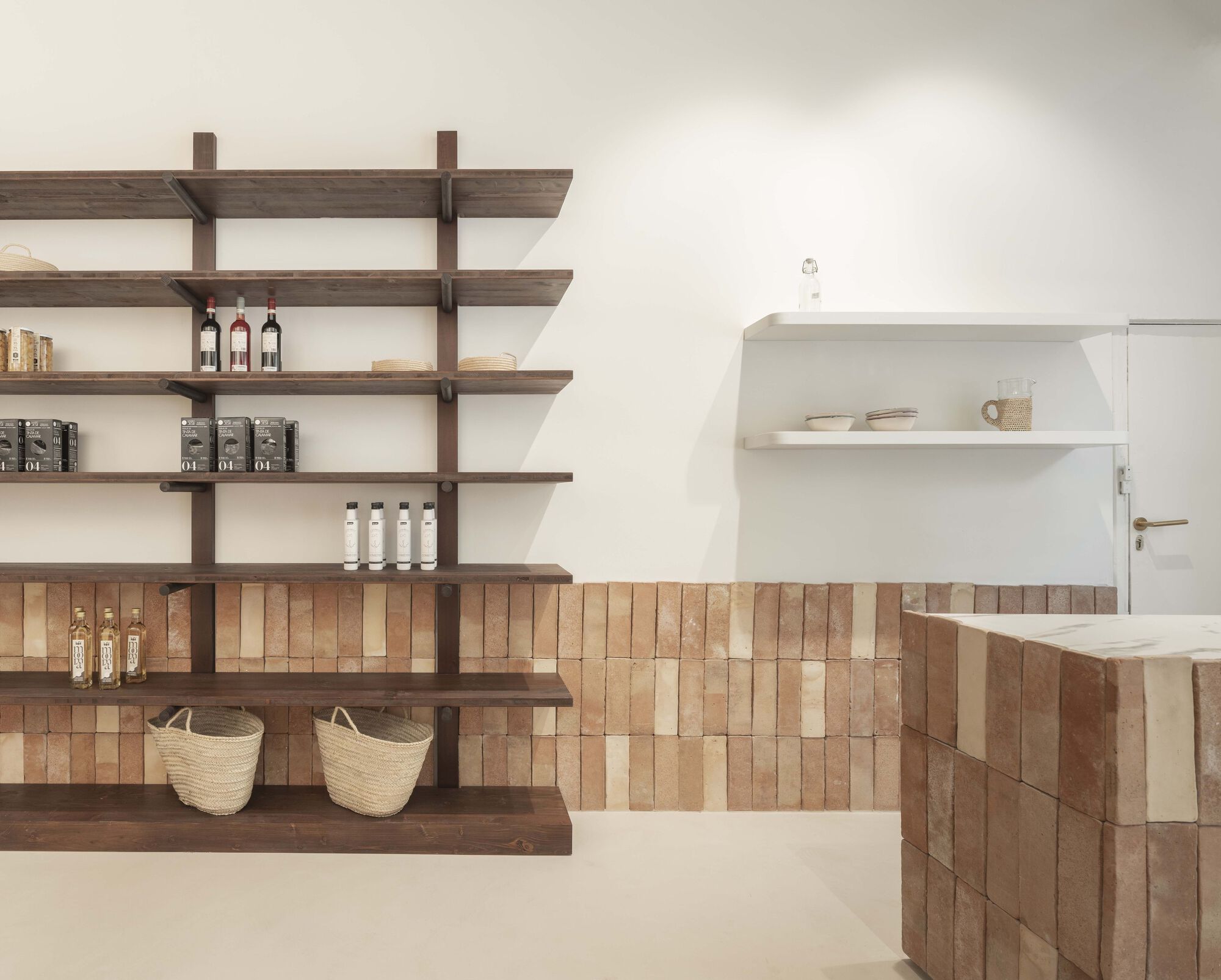 Walnut shelving unit and tiled counter with woven baskets against white walls in soft daylight