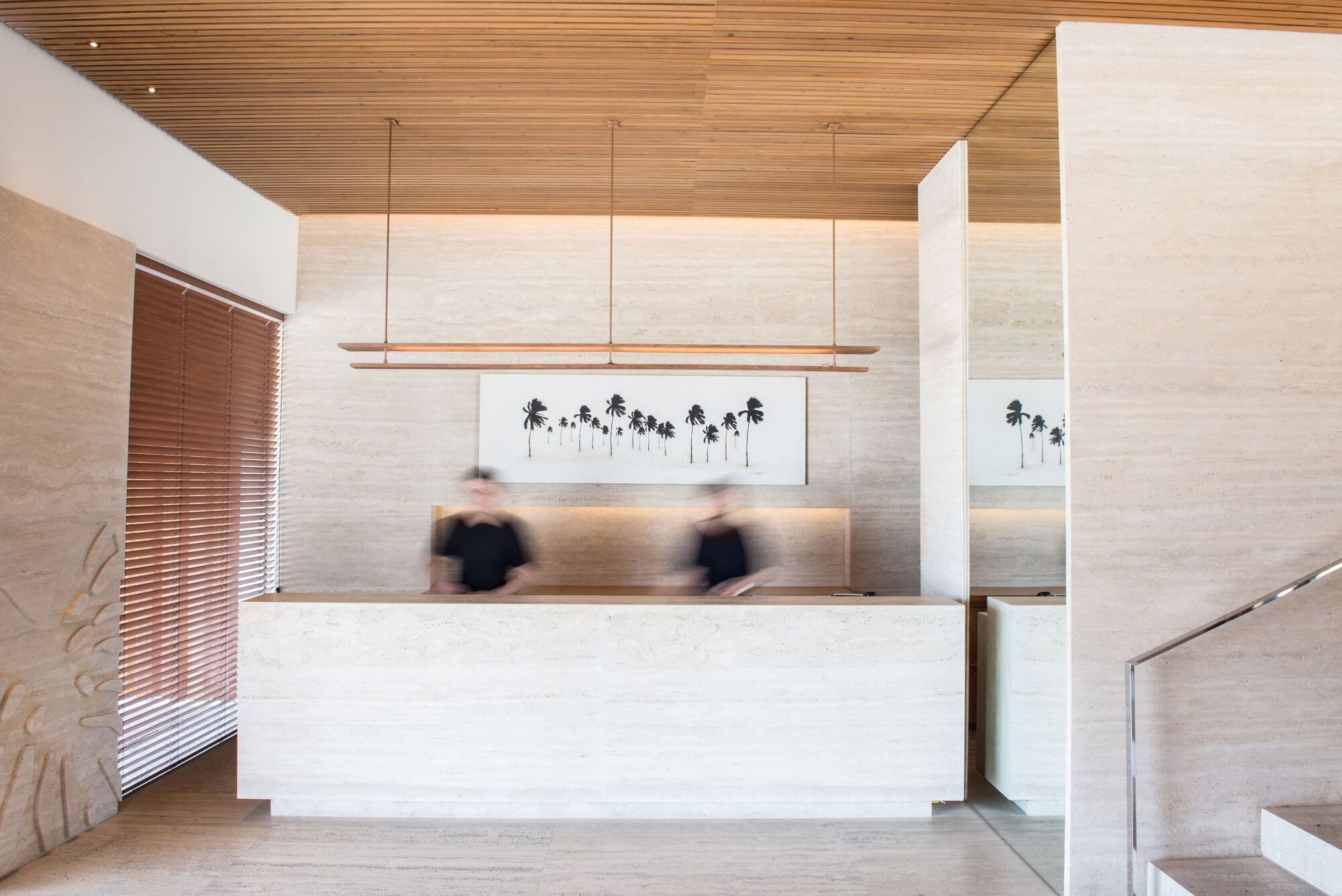 Reception desk with horizontal timber ceiling and blurred figures beneath linear pendant lighting