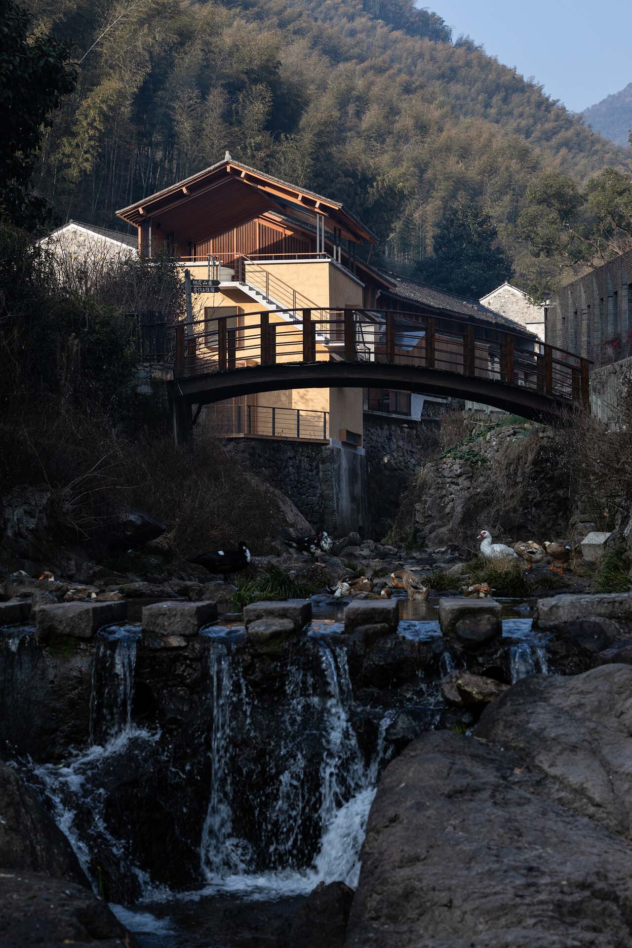 The timber upper story and rammed earth lower volumes spanning the cascading waterfall and rocky streambed