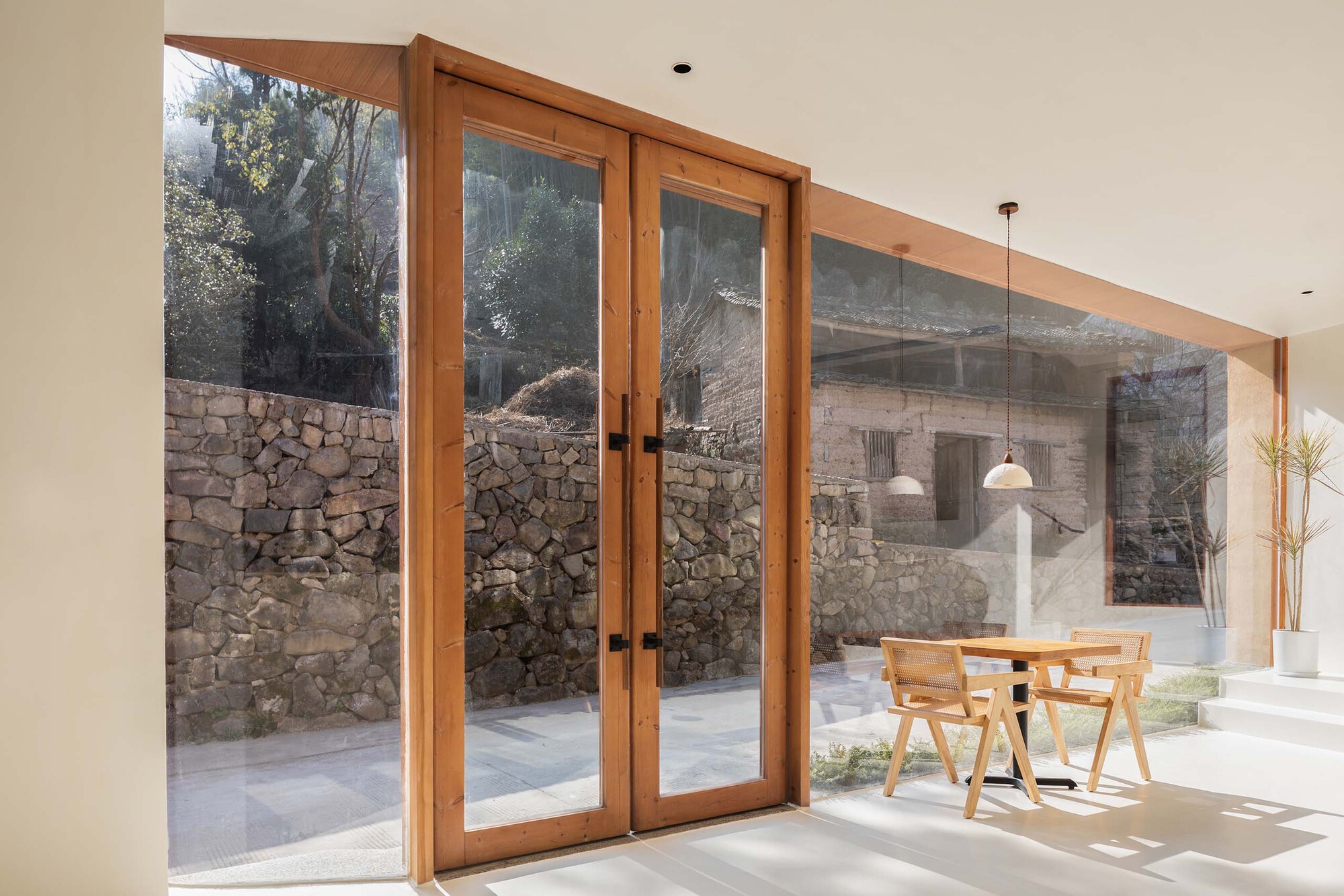 Timber-framed glazed doors opening to a courtyard with stone walls in bright daylight