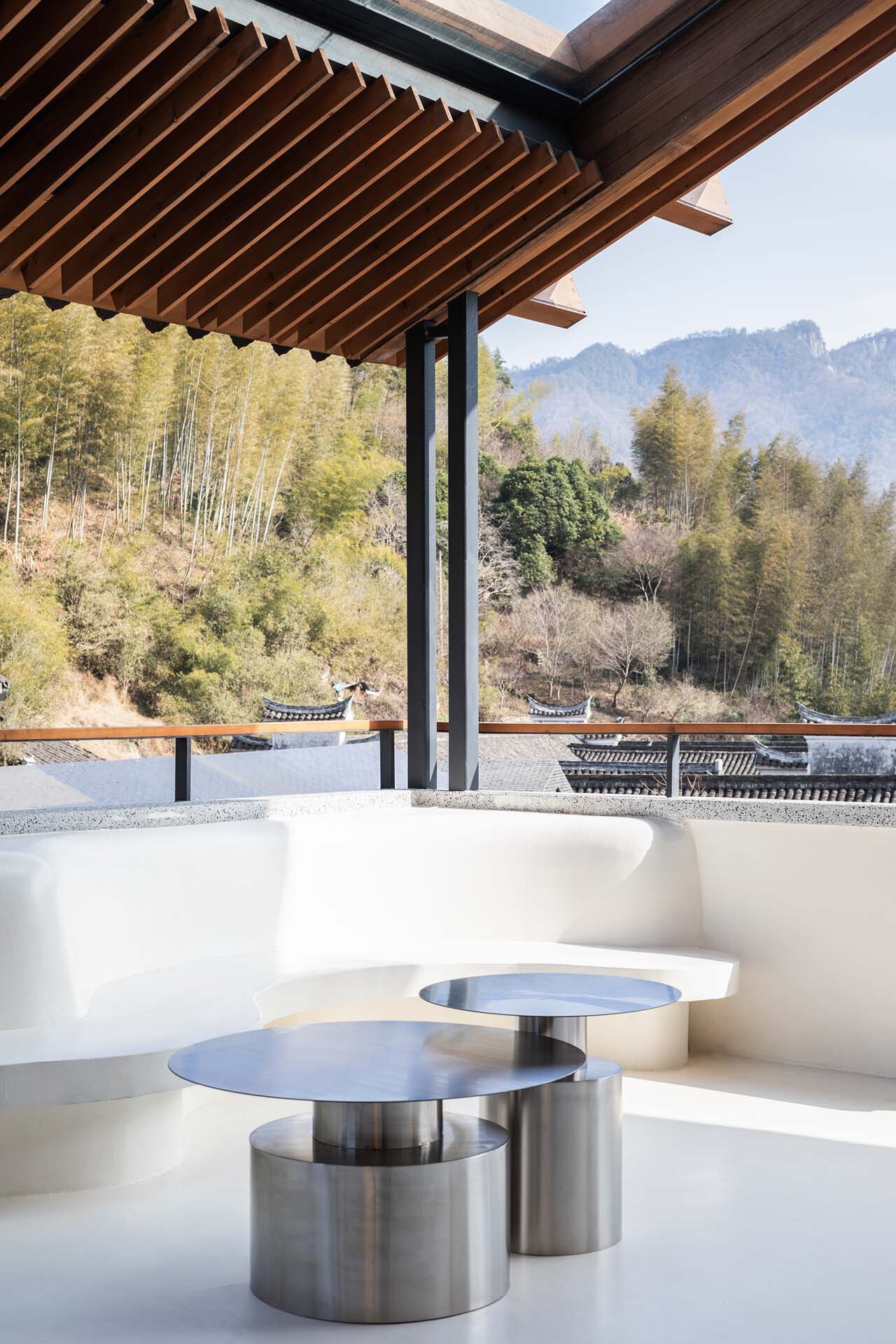 Brushed steel low tables on white terrace overlooking forested hillside in daylight