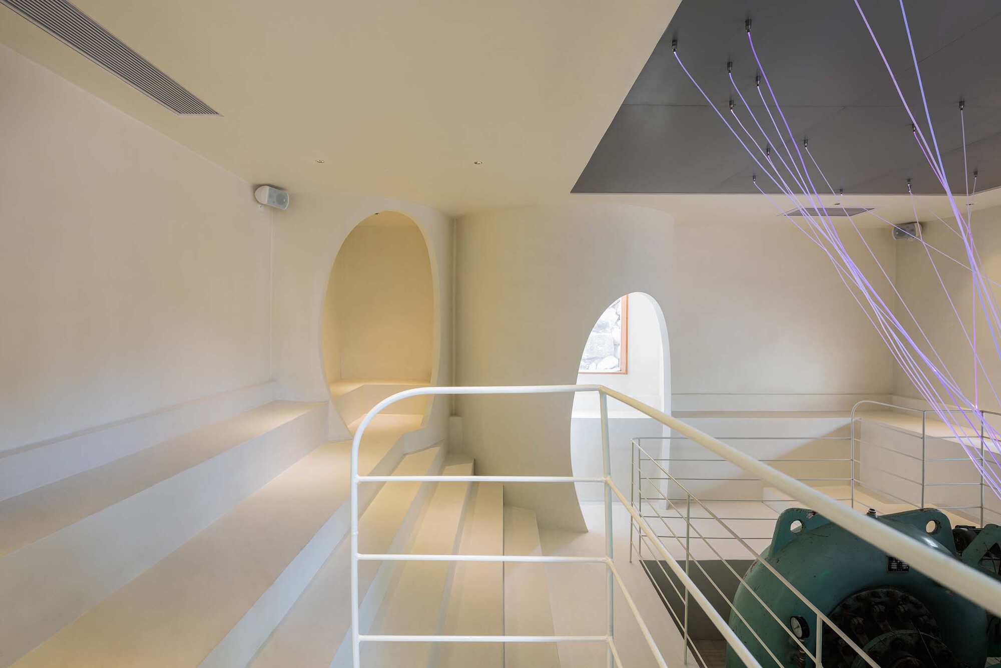 Interior view of white tiered seating with arched doorway and suspended cable lighting from above