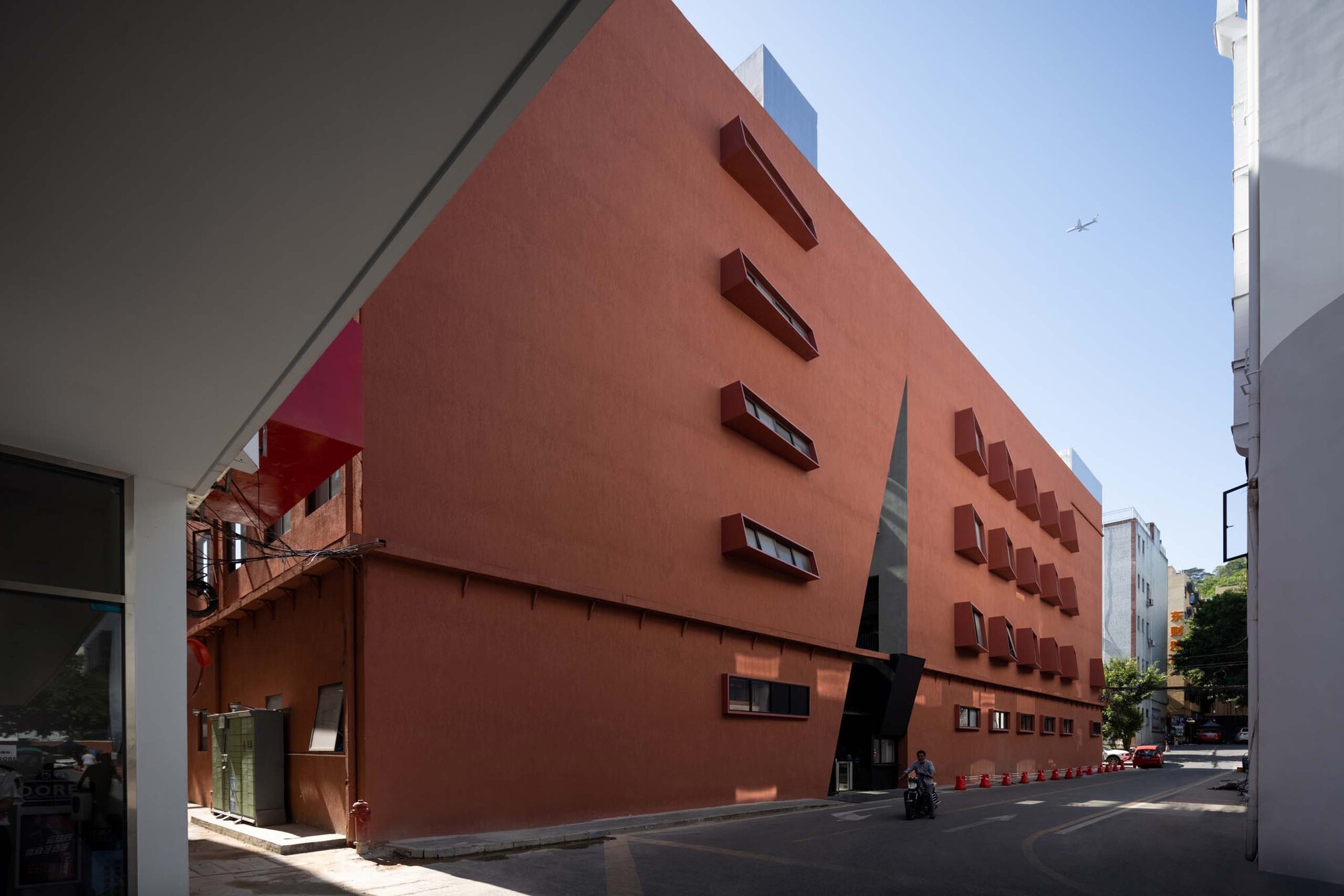 Terracotta-colored facade with projecting window boxes and a diagonal skylight in a narrow urban street