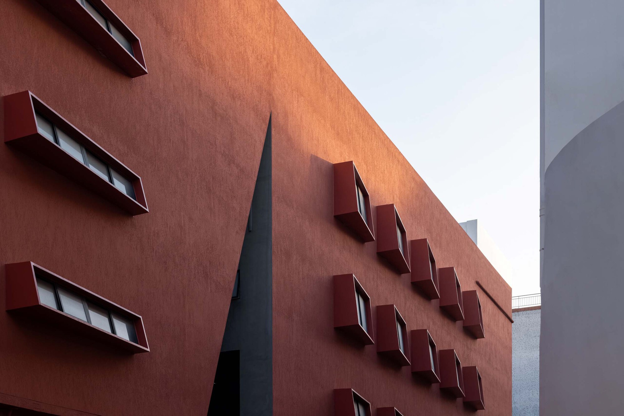 Close-up of the terracotta facade with angled window boxes in two rows and a dark vertical skylight slot