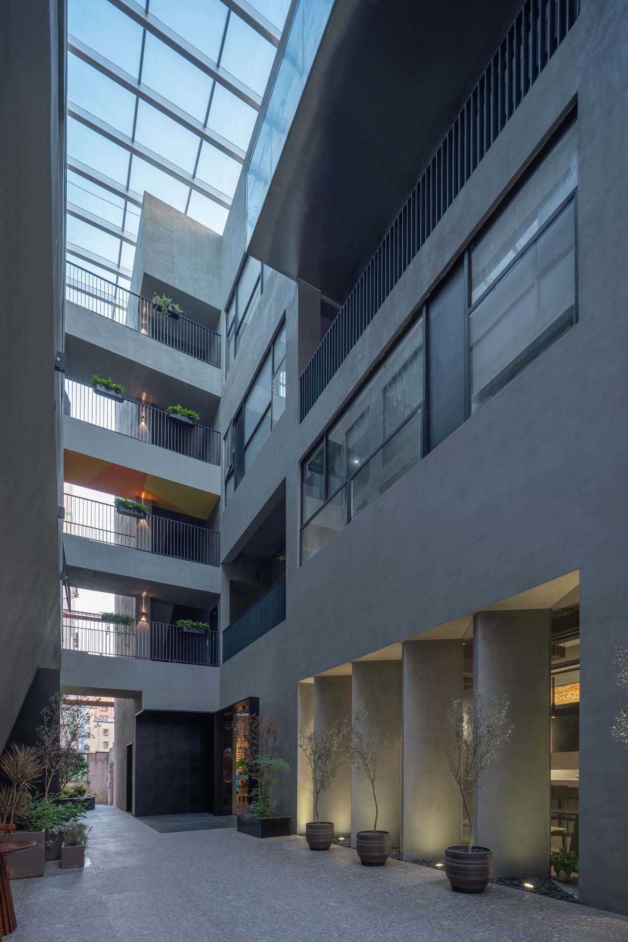 Interior atrium courtyard at dusk with glass skylight, residential balconies and illuminated ground-floor planters