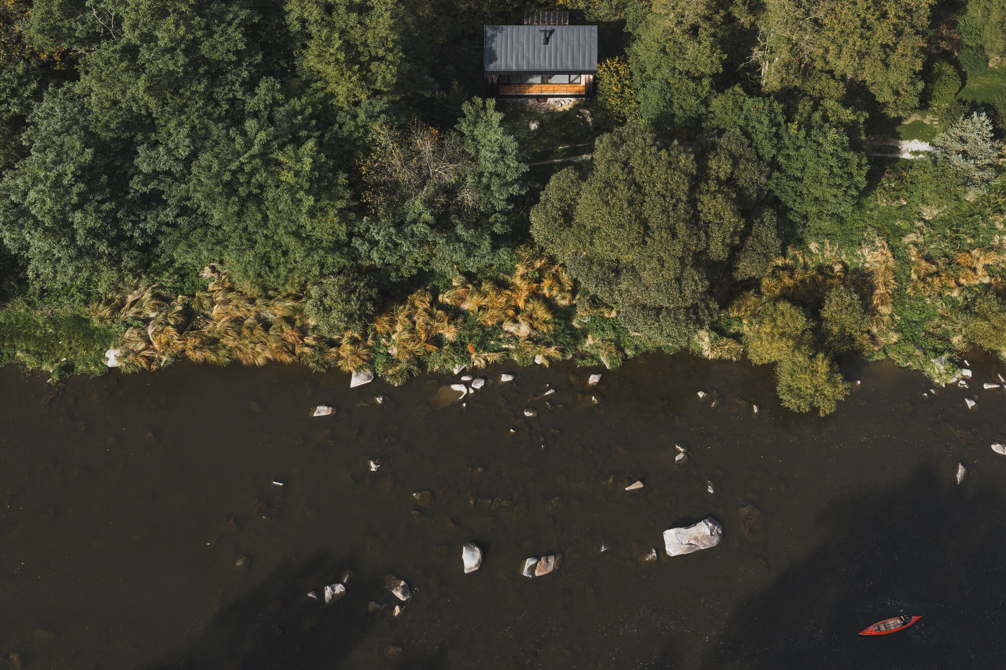 Aerial view of the timber cabin cantilevered above a rocky shoreline with kayaker below