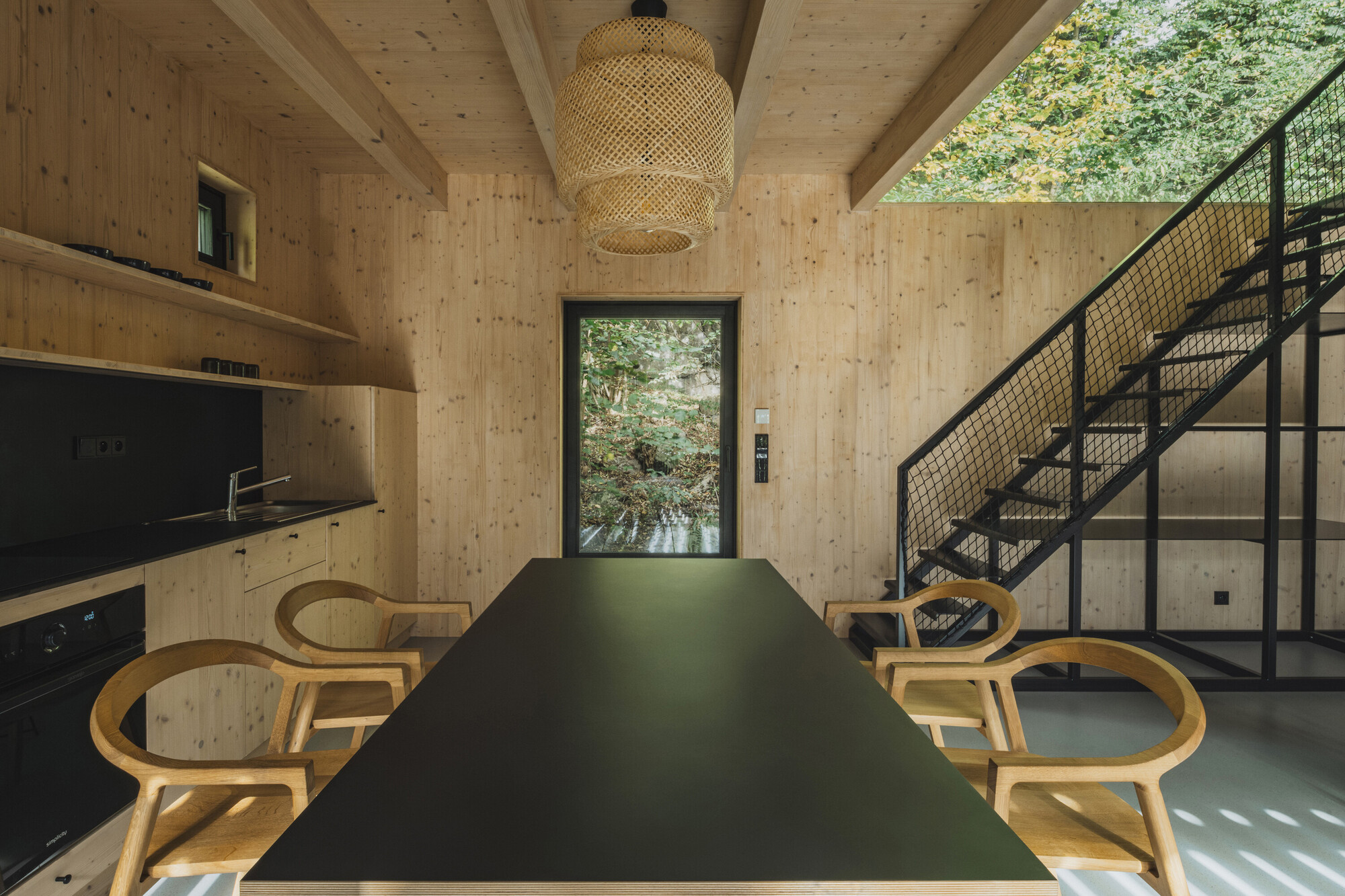 Long dining table with bentwood chairs beneath woven pendant facing doorway to exterior