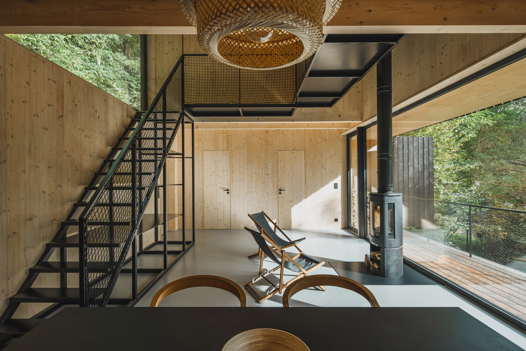 Living area with mesh-infill staircase, wicker light fixture, and glazed opening to timber deck