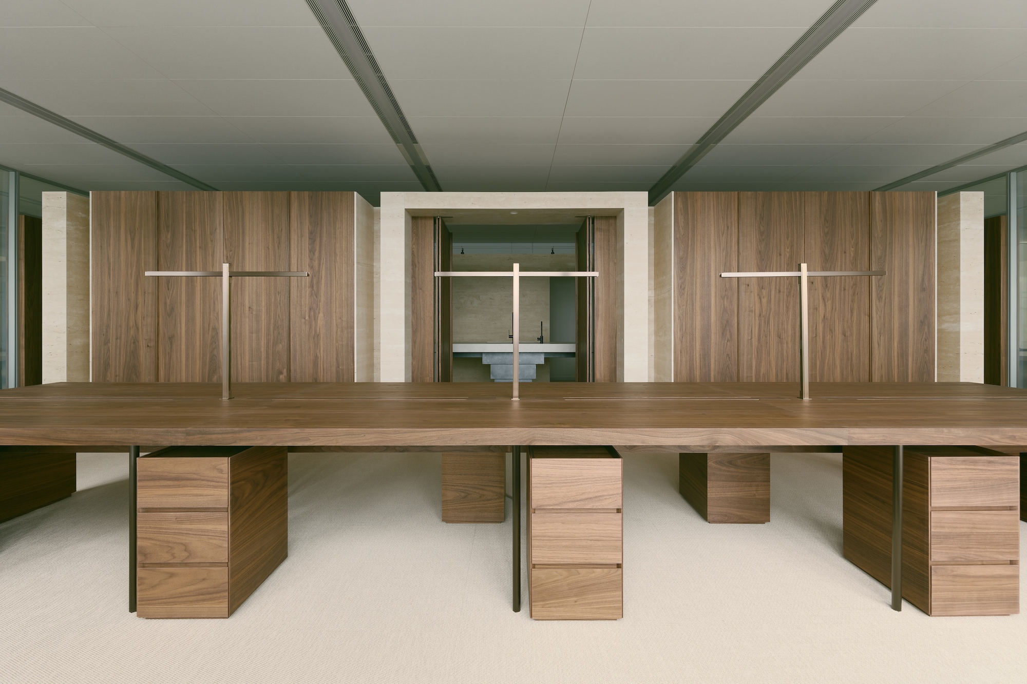 Long workspace with walnut desks and steel legs beneath a timber-clad wall with recessed lighting