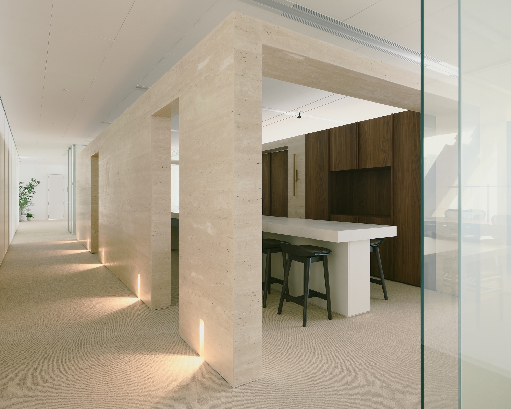 Light travertine portal framing a kitchen bar with uplighting along the floor and walnut cabinetry