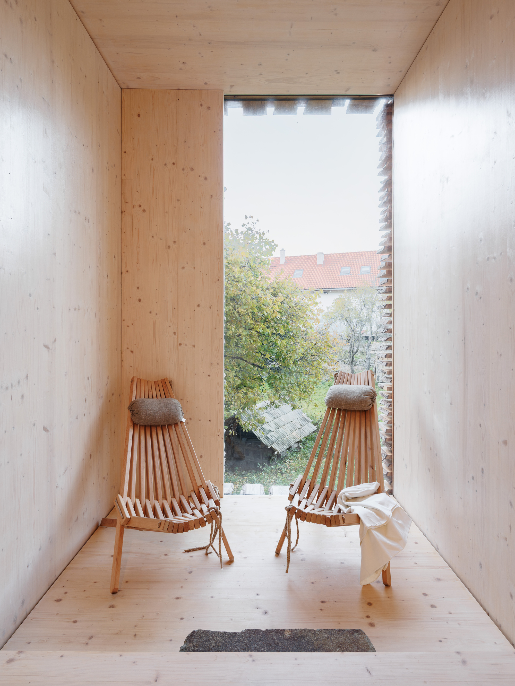 Two timber lounge chairs facing tall window opening to garden view through slatted screen