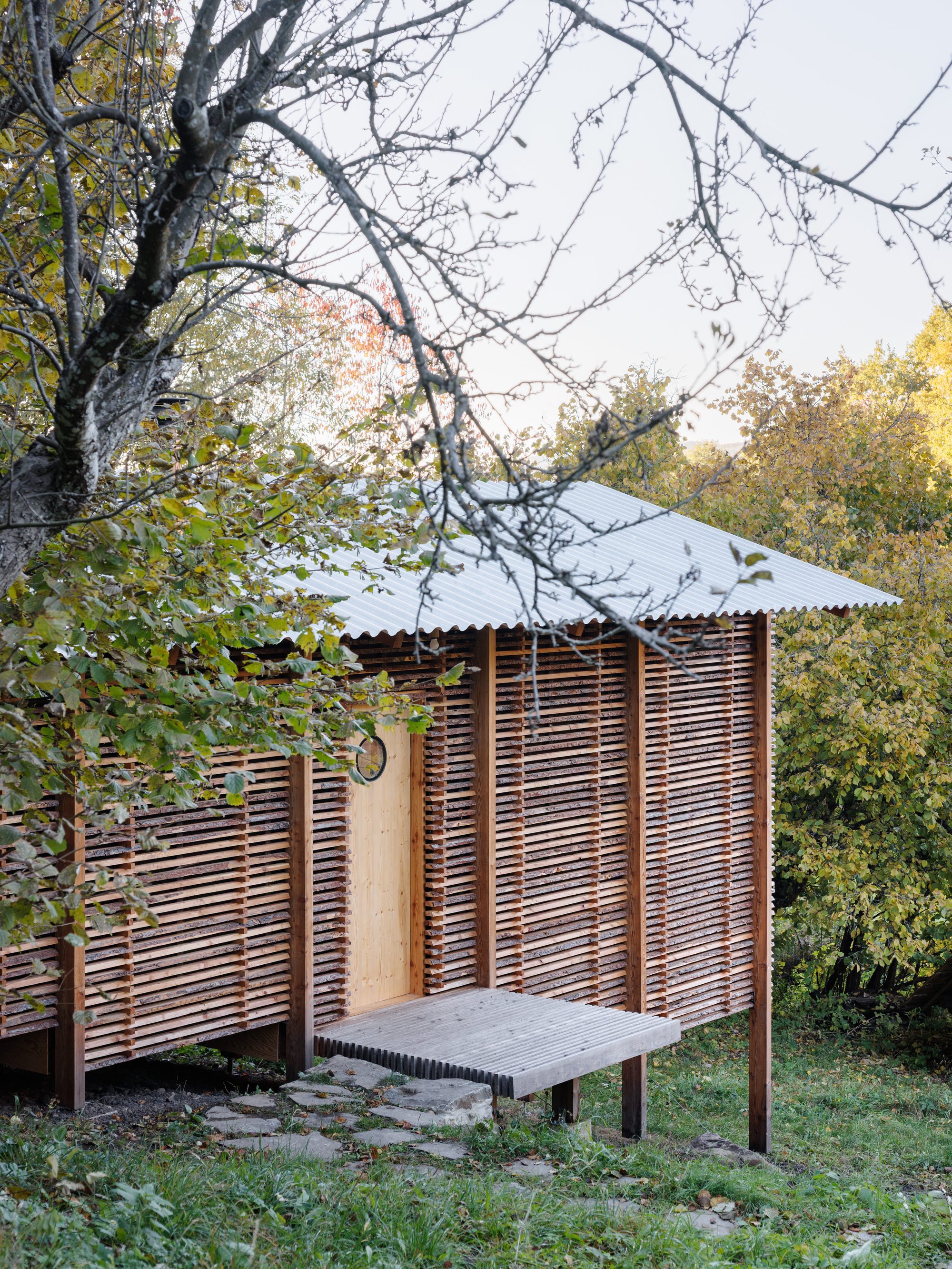 Corner of the horizontal slat facade with corrugated metal roof and outdoor bench under bare branches
