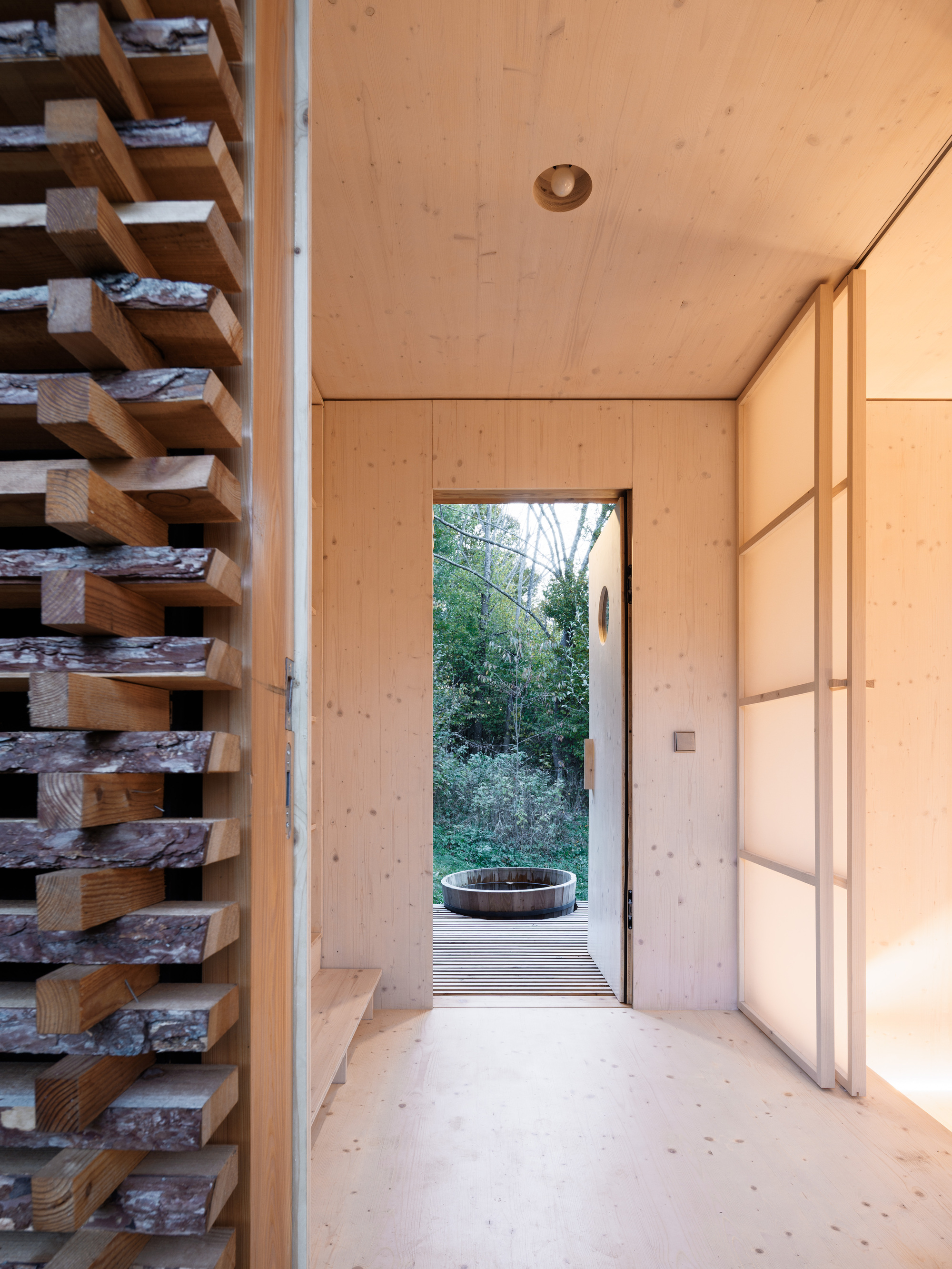 Interior hallway with plywood walls, ceiling, and floor looking toward open doorway framing wooden barrel outside