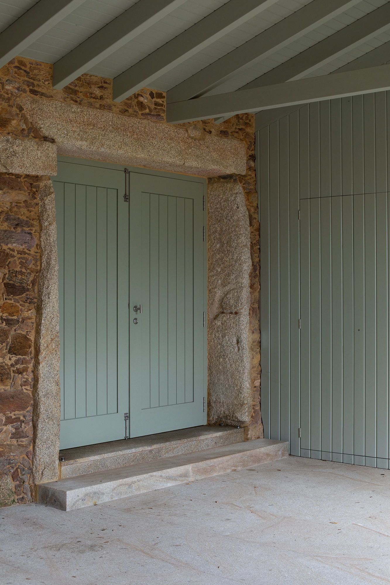 Painted timber double doors set within rough granite frame and stone threshold under pitched ceiling
