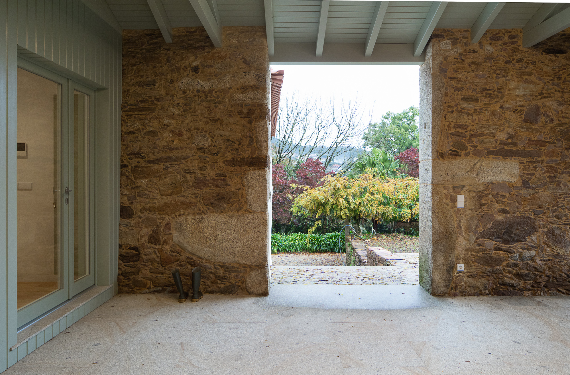 Covered entrance passage with exposed stone walls and painted timber ceiling beams framing a garden view