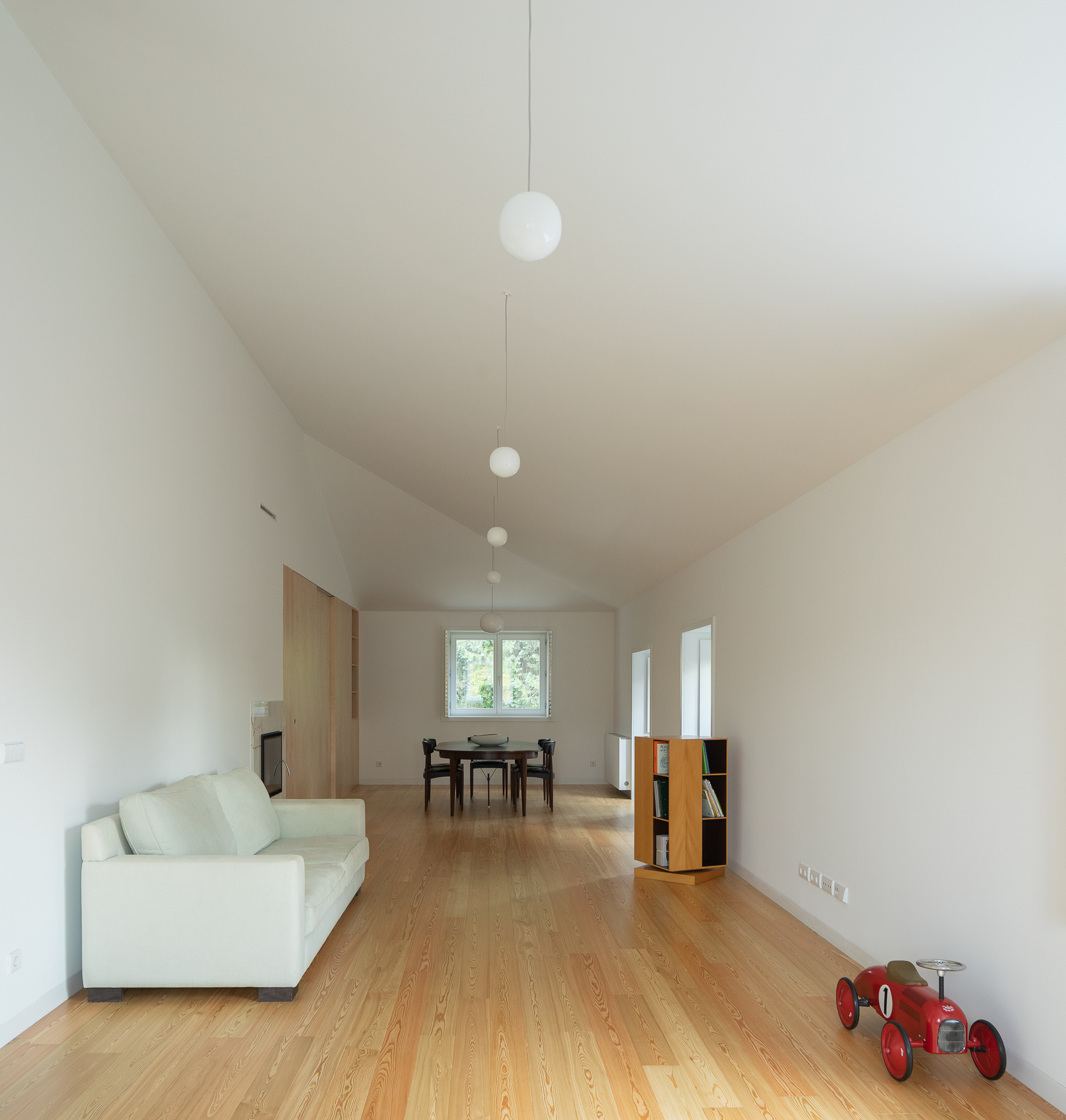 Open living space with oak flooring, vaulted ceiling and pendant lights suspended in a row