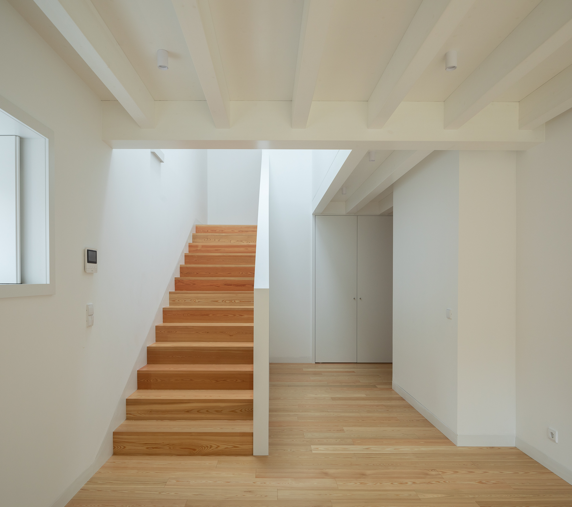 Timber staircase with exposed ceiling beams rising through a double-height volume with wood flooring