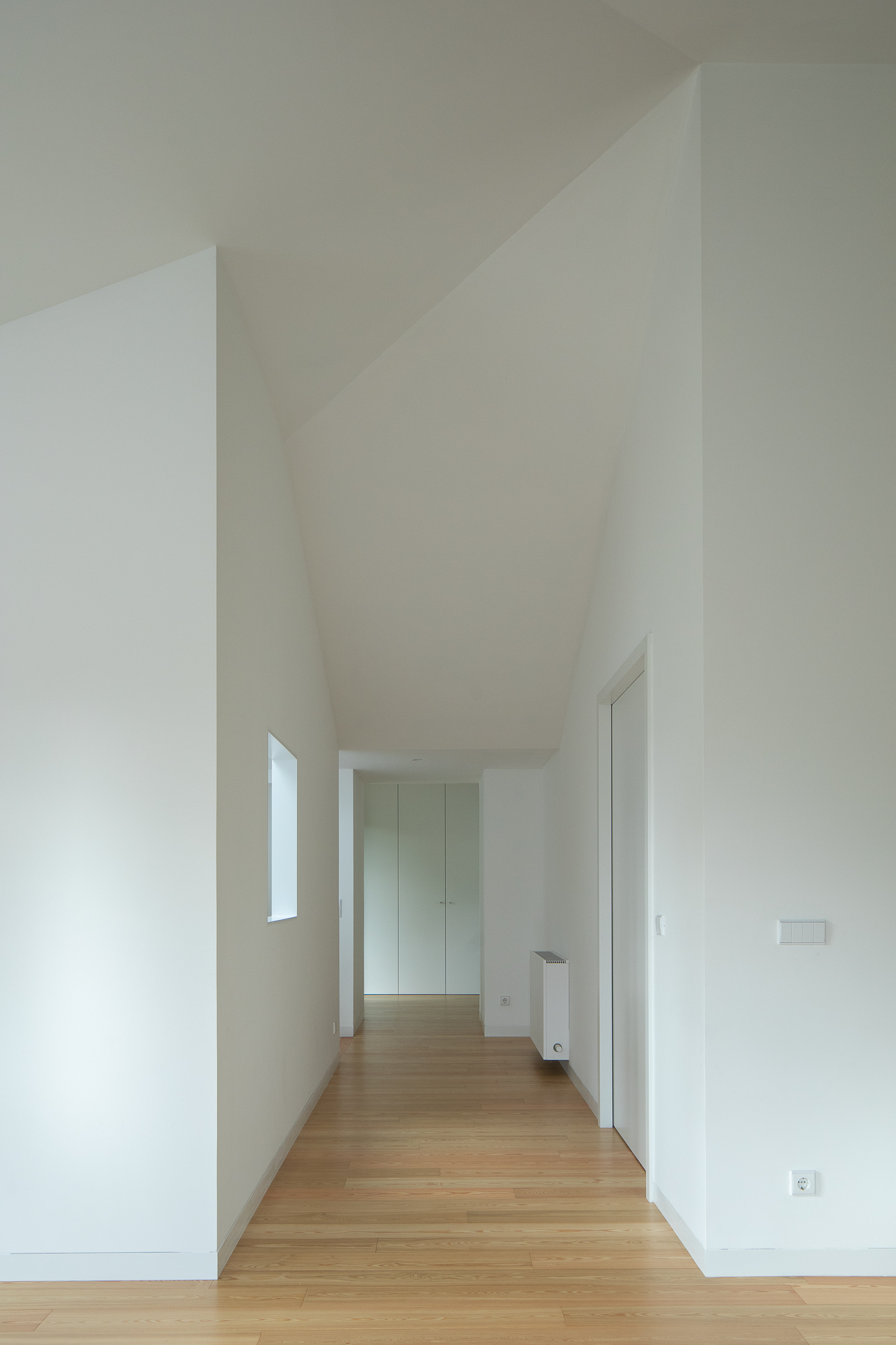 Corridor with angled ceiling planes, oak flooring, and tall vertical window casting natural light