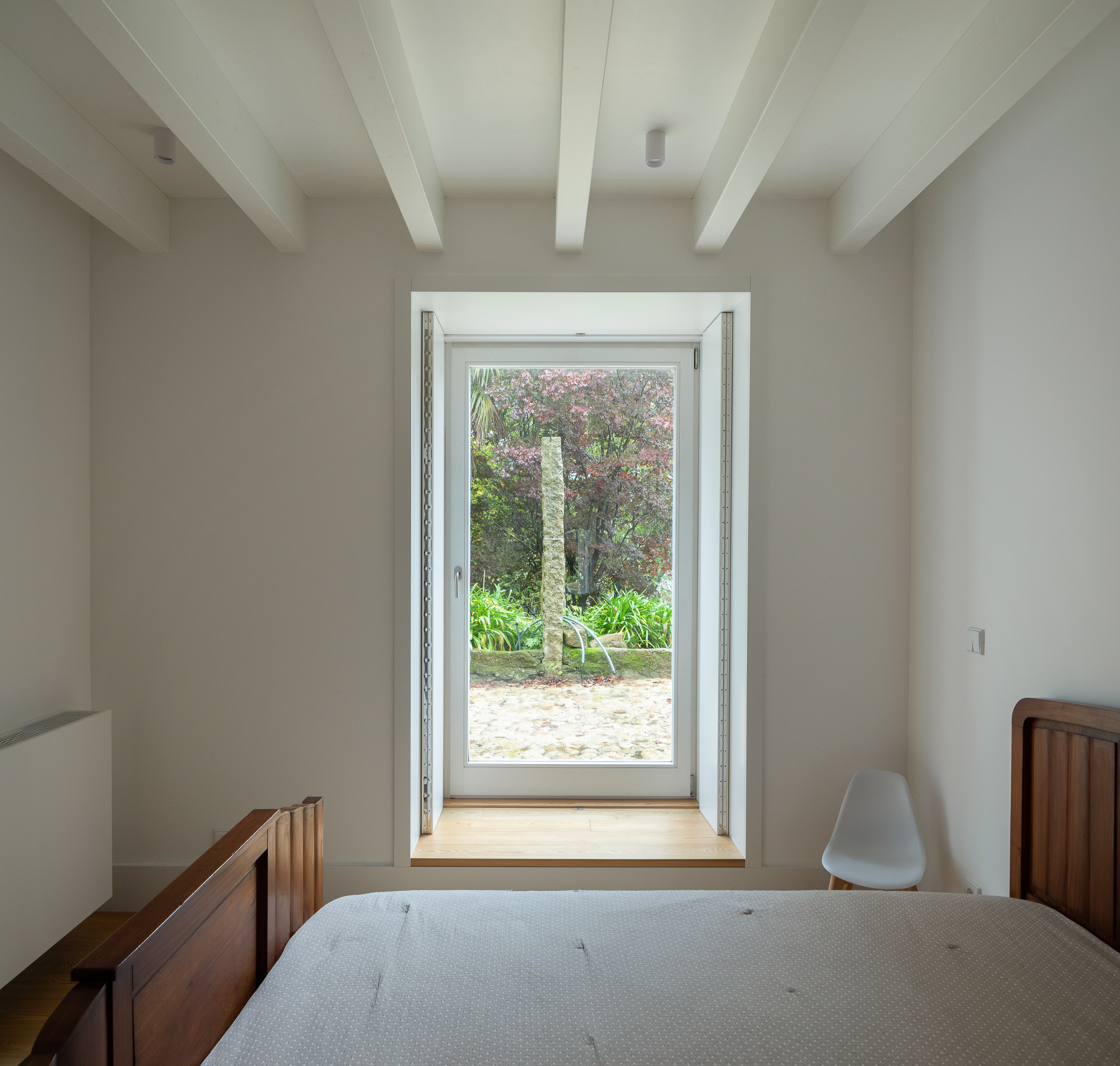 Bedroom with exposed white beams and framed door opening to garden courtyard with palm tree