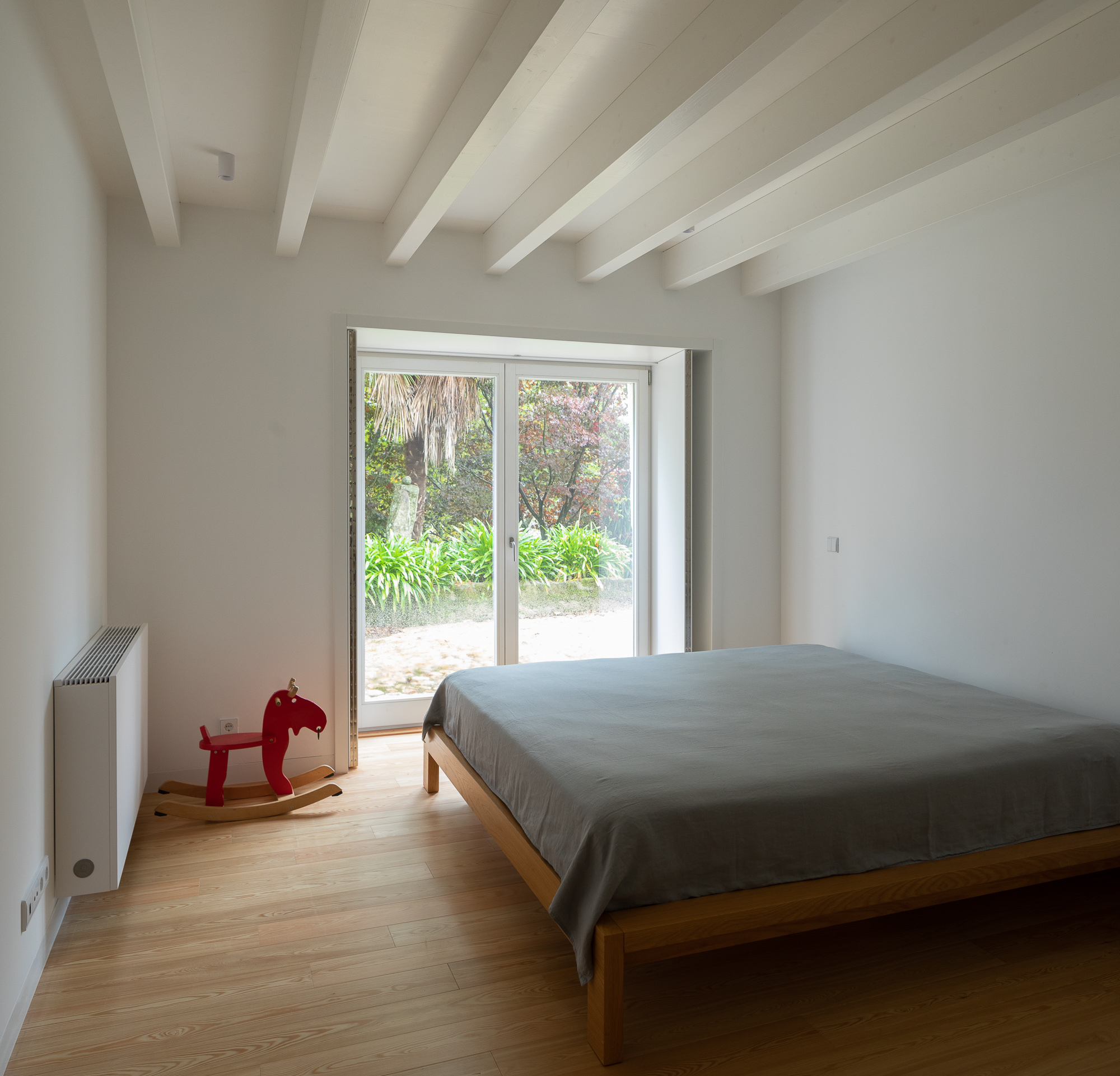 Bedroom with timber platform bed and double glass doors framing view of garden vegetation