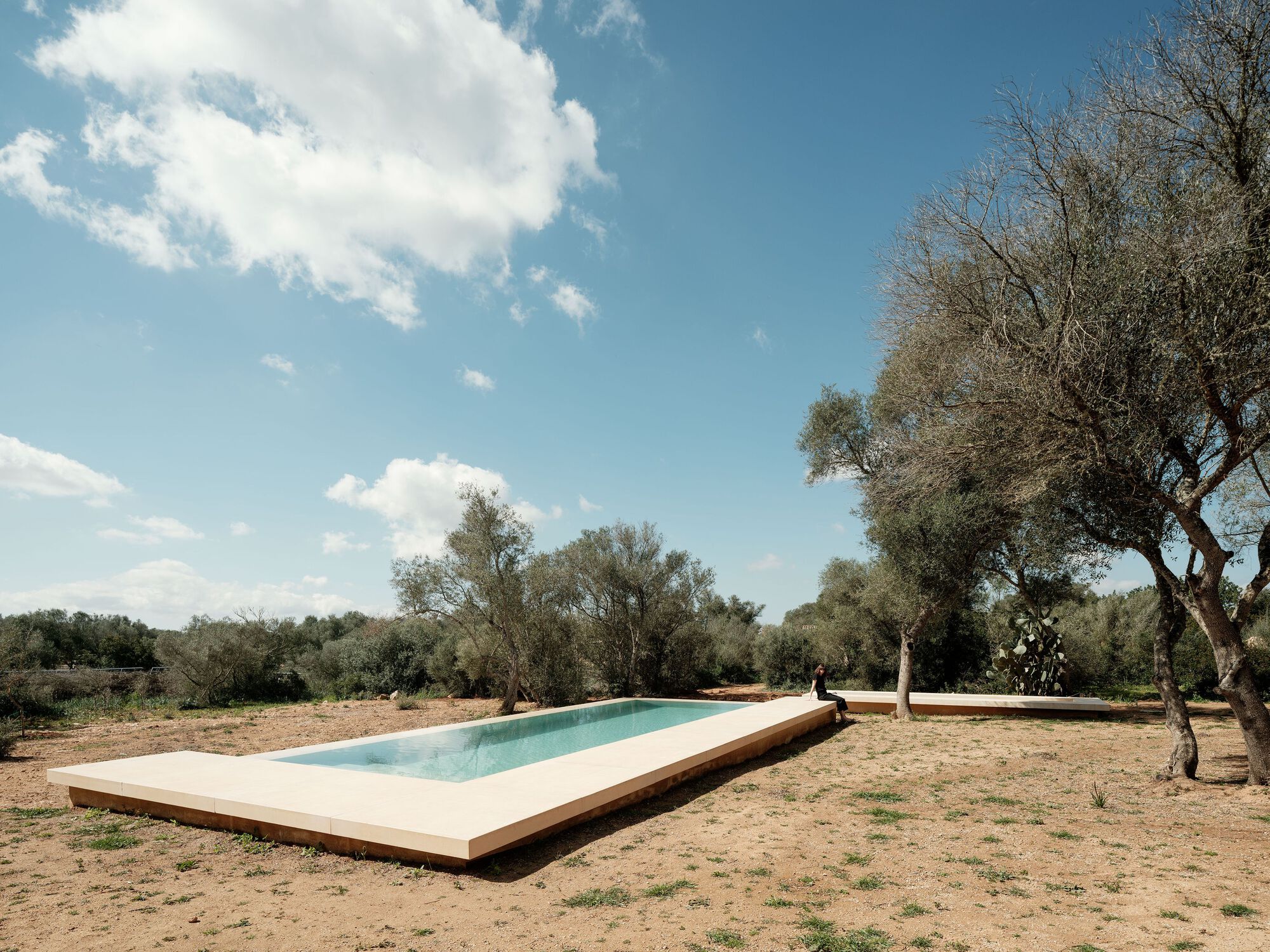 Elevated rectangular swimming pool set in dry landscape under blue sky with scattered clouds