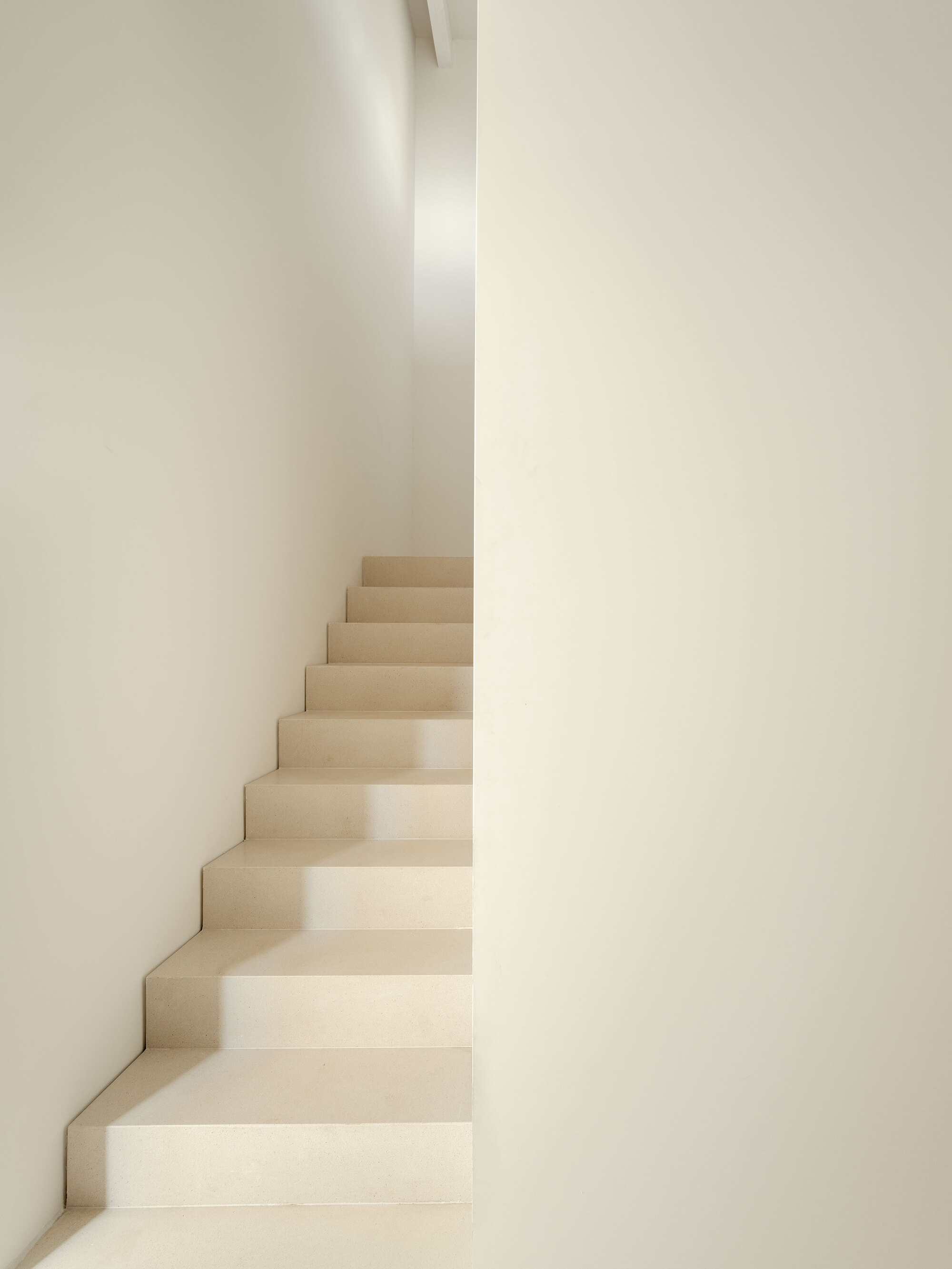 Narrow plastered staircase between converging white walls in soft natural light