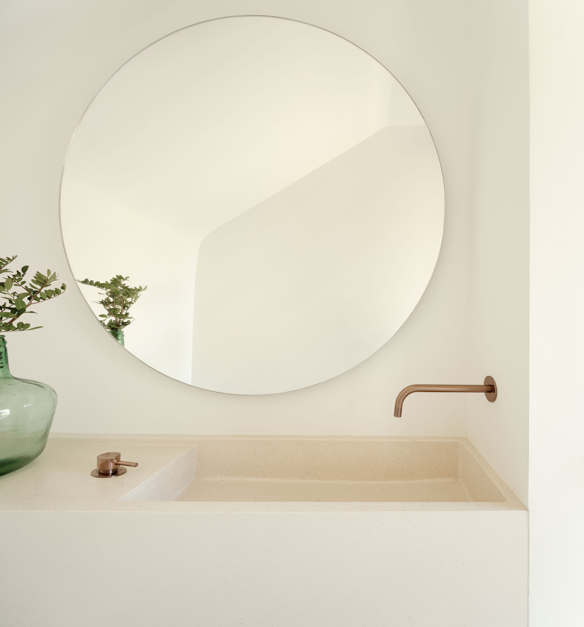 Bathroom vanity with integrated stone basin, round mirror, copper faucet, and glass vase
