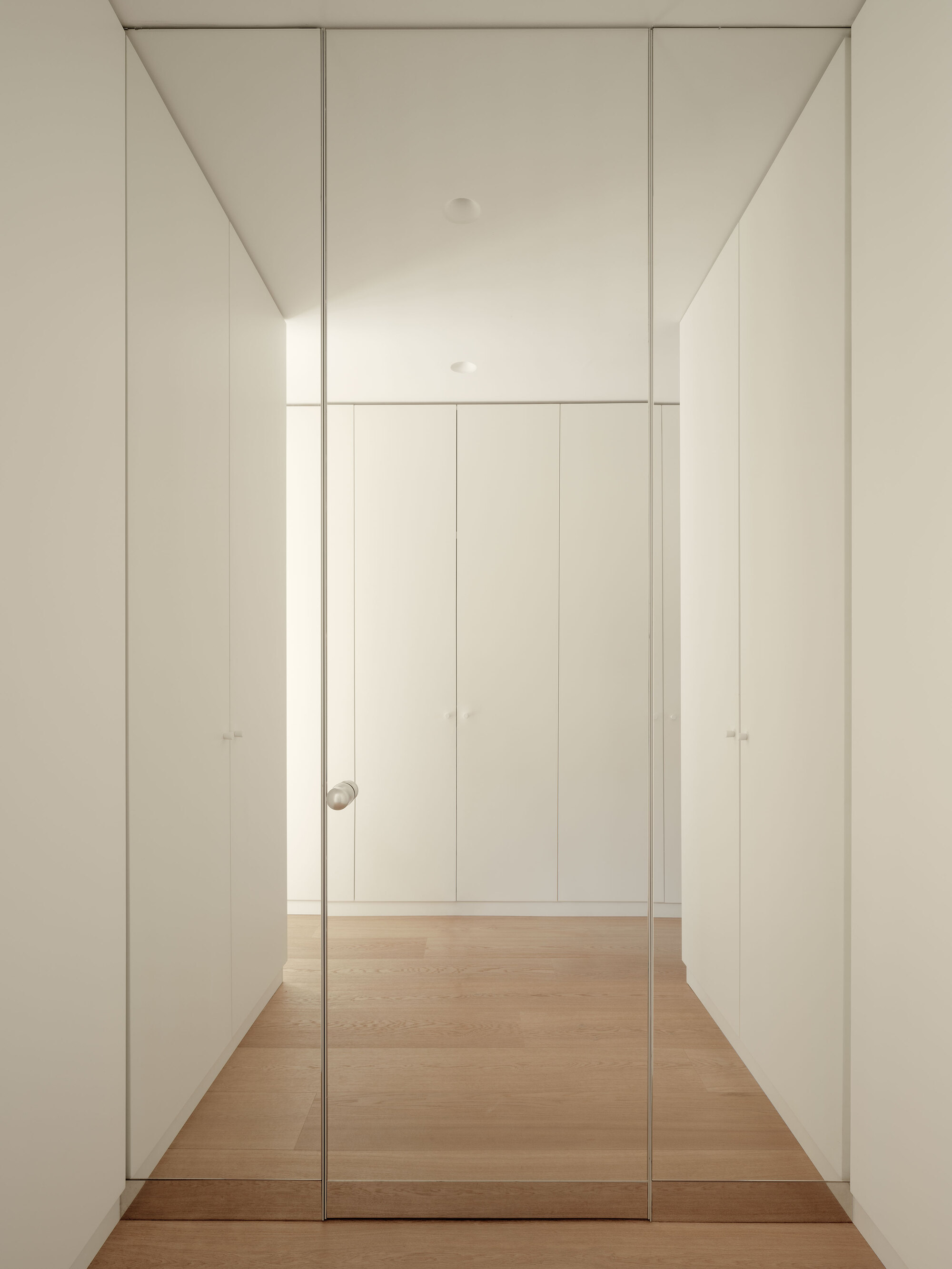 Hallway with floor-to-ceiling white storage panels and full-height glazed door on timber flooring
