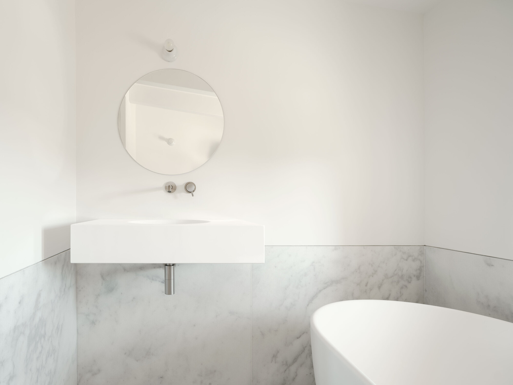 Wall-mounted rectangular basin with circular mirror above marble wainscoting in a corner