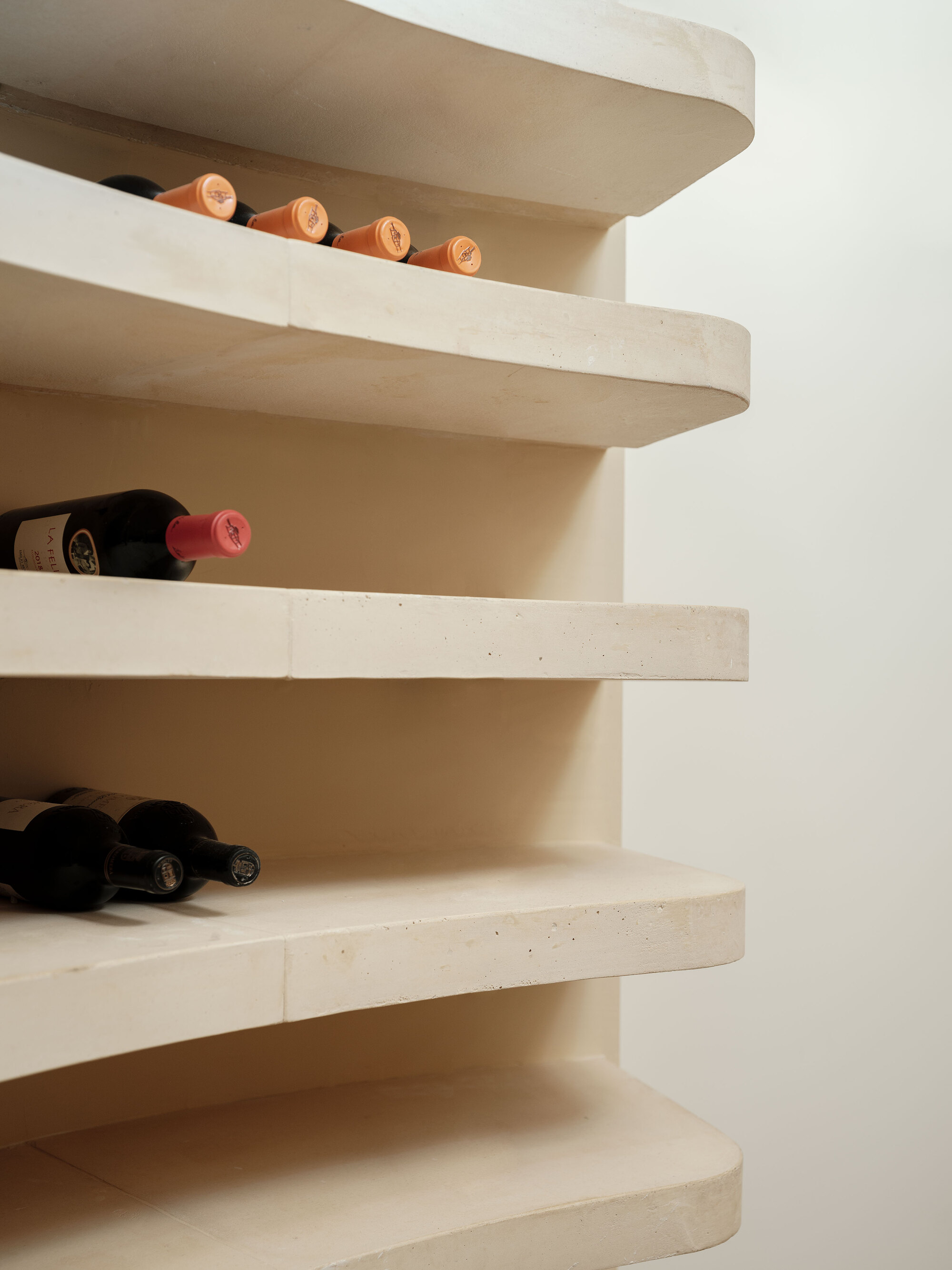 Curved cantilevered stone shelves forming a wine rack with bottles resting on pale treads