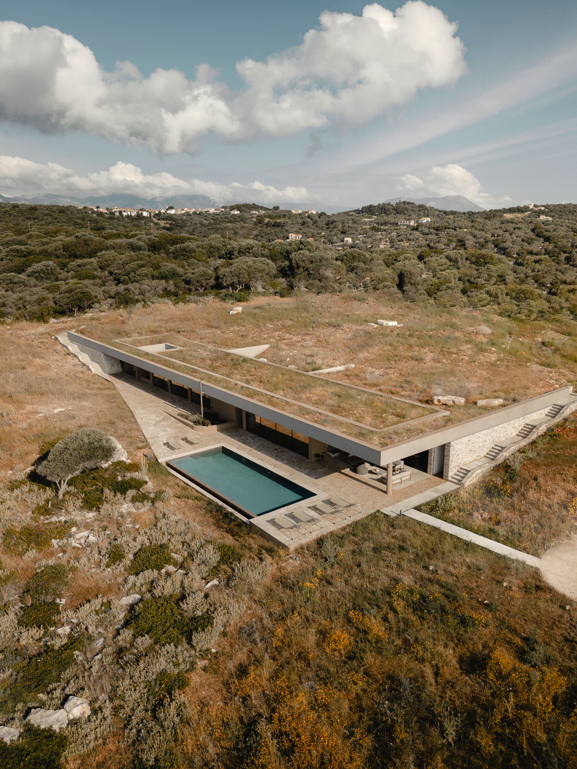 Drone view showing planted roof terrace and swimming pool terrace embedded in hillside with forested valley beyond