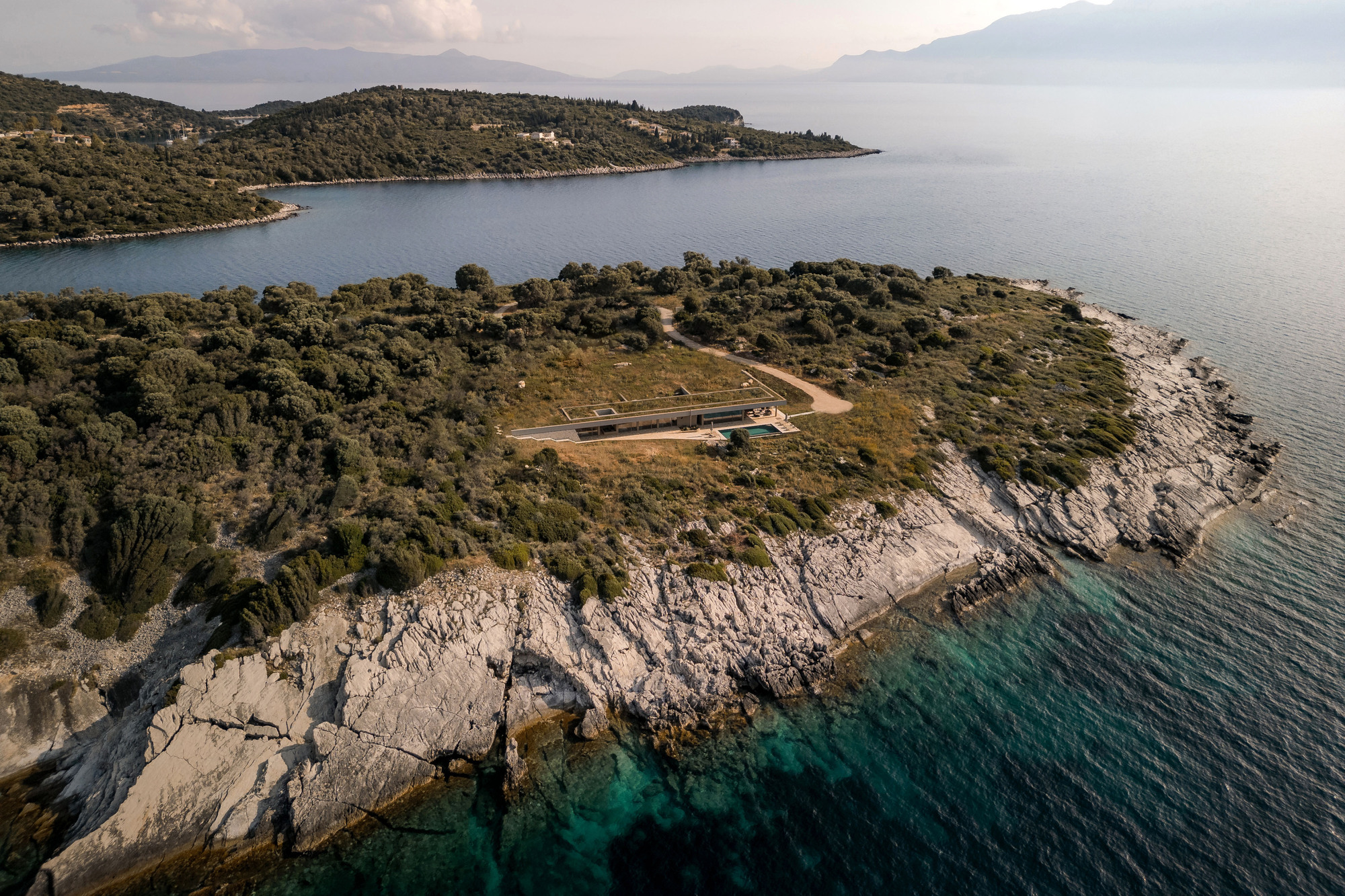Aerial view of a low horizontal structure nestled on a rocky coastal peninsula with turquoise waters