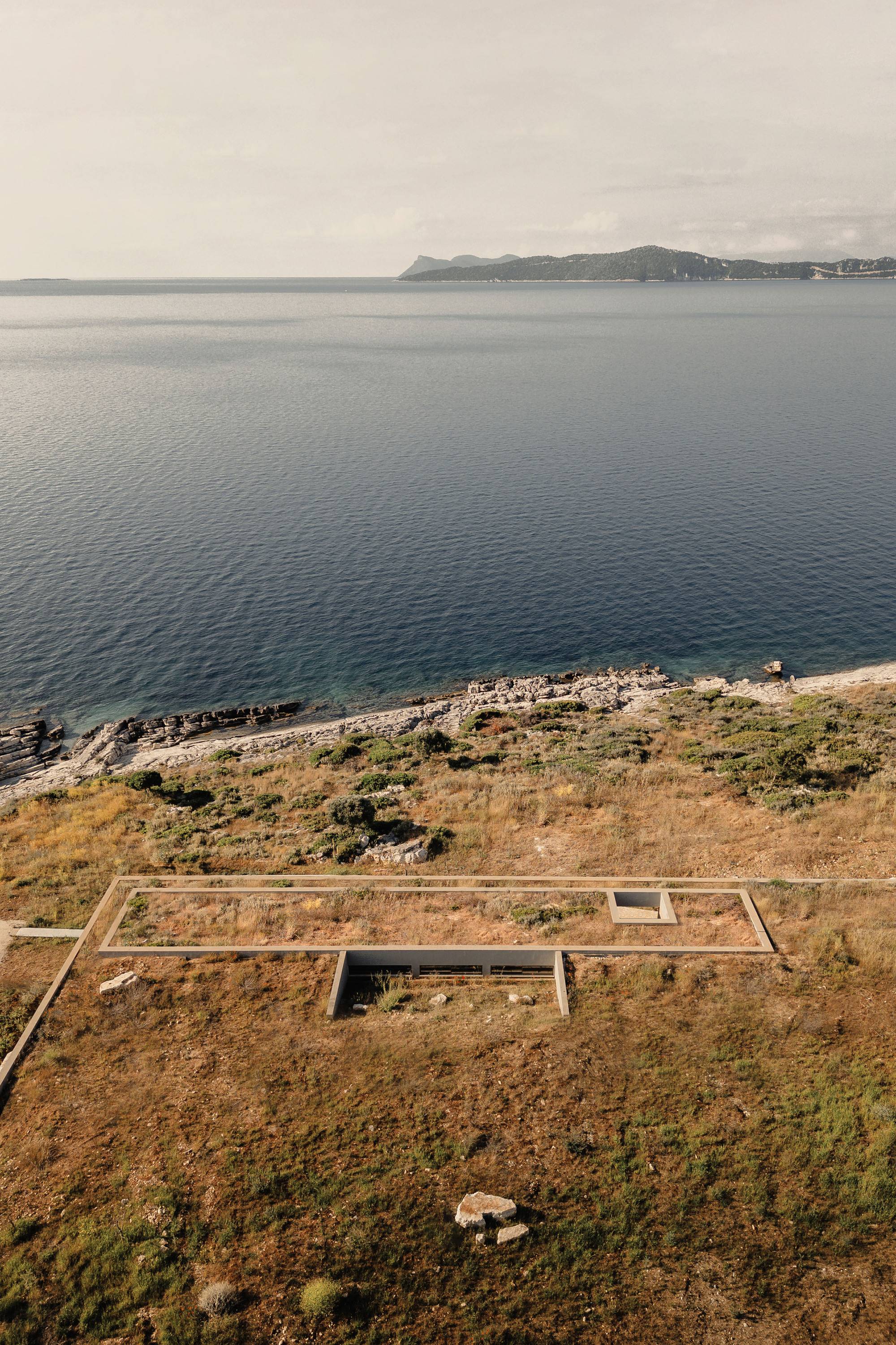Drone view of the rectilinear foundation and terrace platform set into dry scrubland above the sea