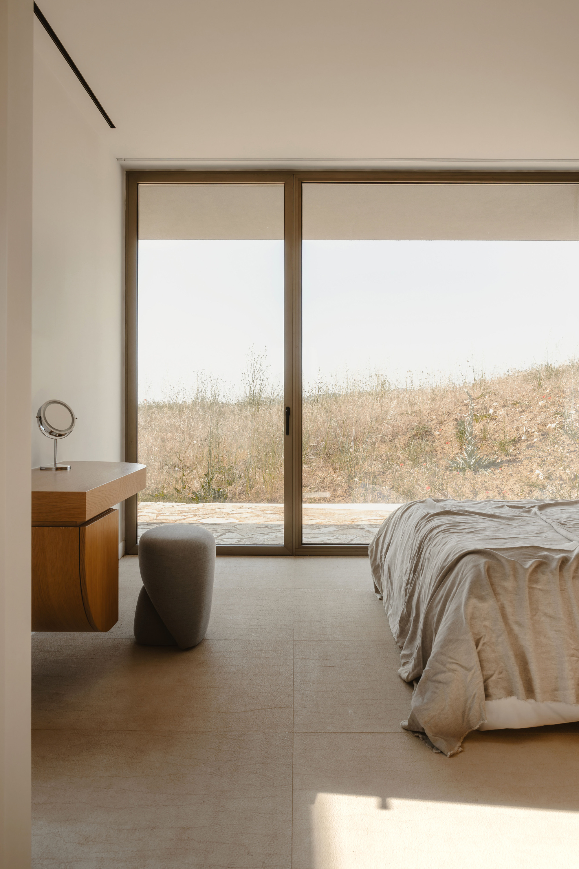 Bedroom interior with sliding glass doors framing a view of dry golden grasses beyond a concrete terrace