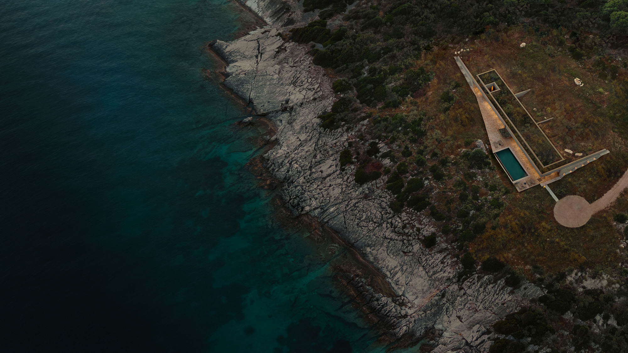 Aerial view of the rectangular pool terrace on a rocky coastal headland with dark blue water