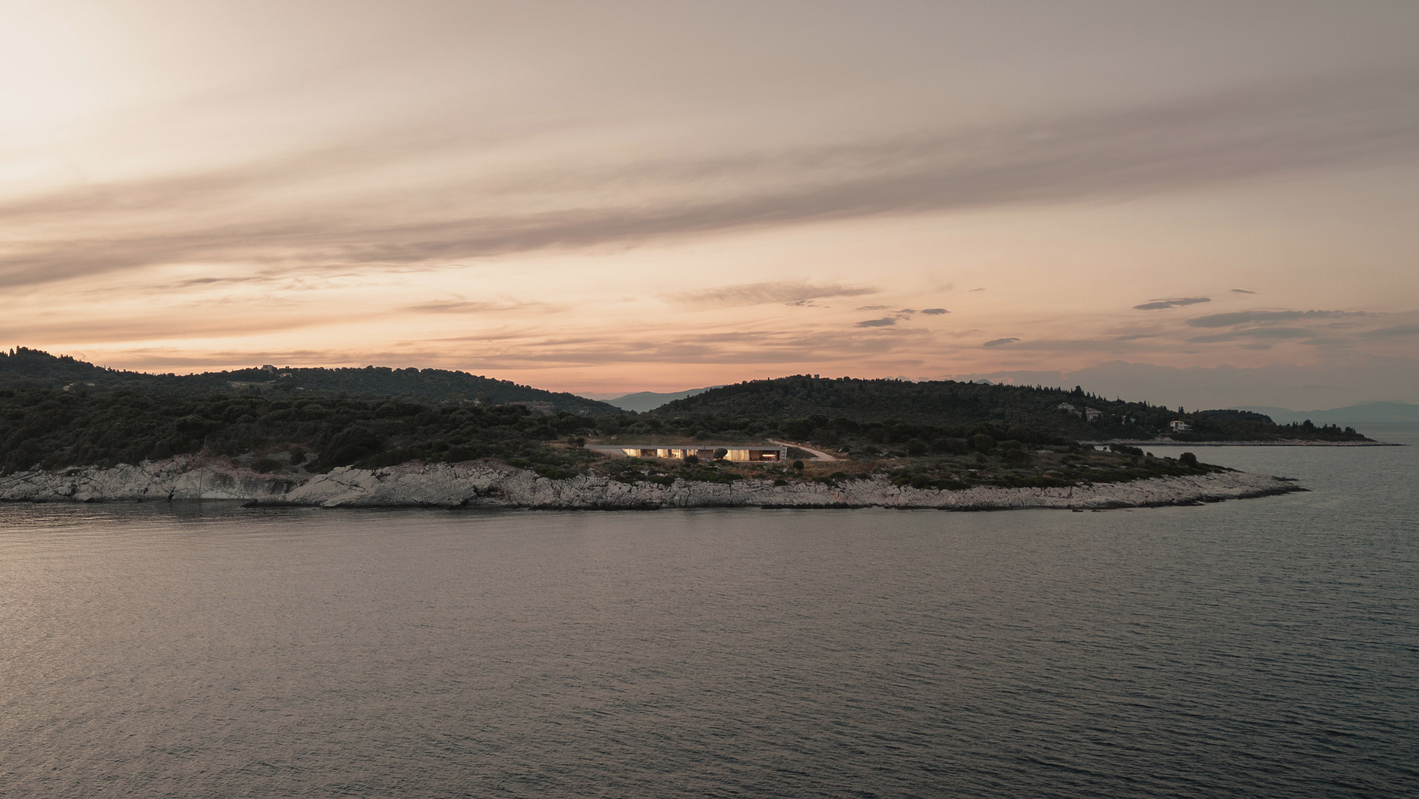 Distant view of a low horizontal structure nestled on a rocky coastline at sunset