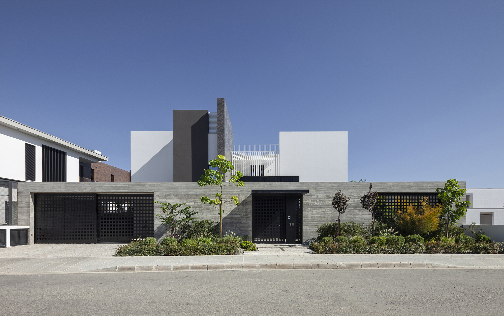 Street view of the facade with perforated metal garage doors and horizontal timber cladding beneath white volumetric forms