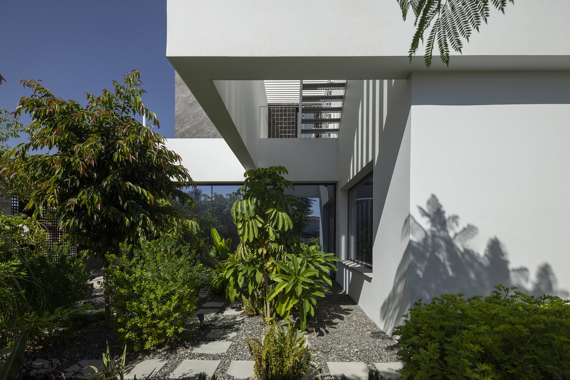 Cantilevered upper volume extending over landscaped courtyard with planted trees and gravel ground surface