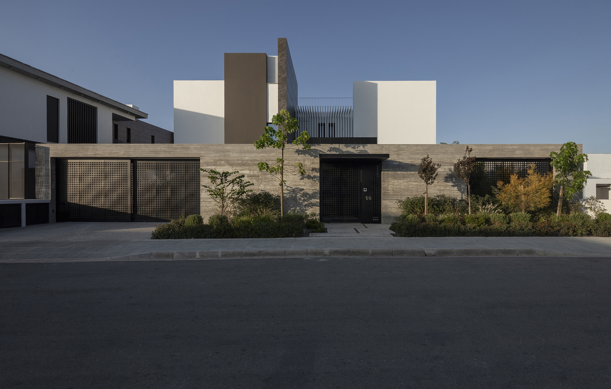 Street view of the perforated metal fence and black entrance door set within a horizontal stone wall