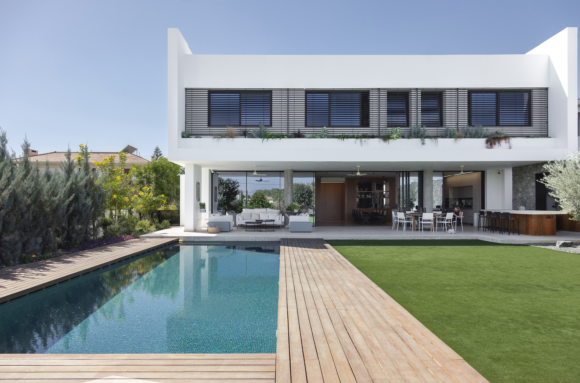 Rear elevation with upper balcony louvers and open ground floor terrace overlooking the swimming pool and lawn
