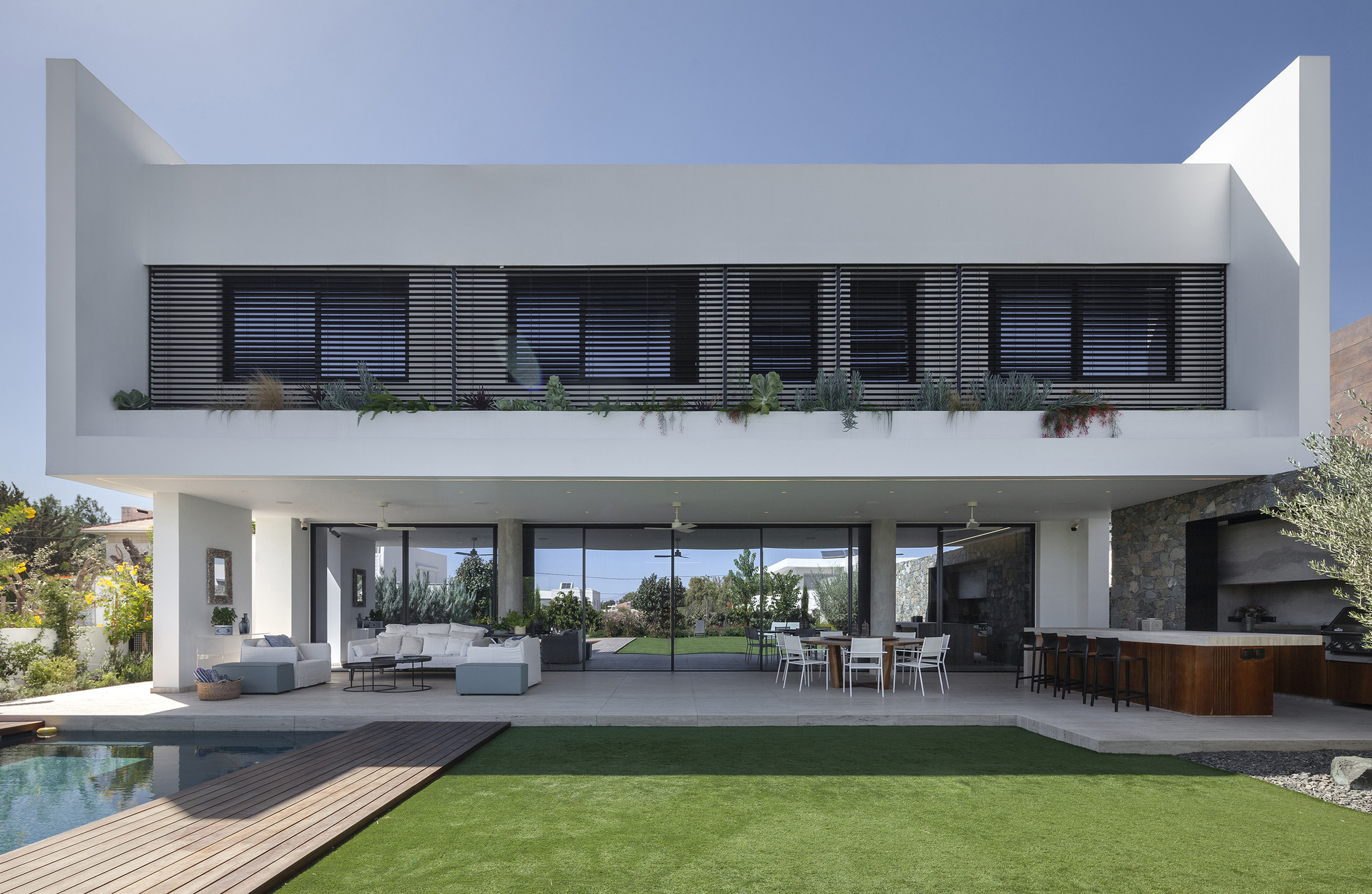 Garden facade showing horizontal louvers on the upper balcony above the open living terrace and pool