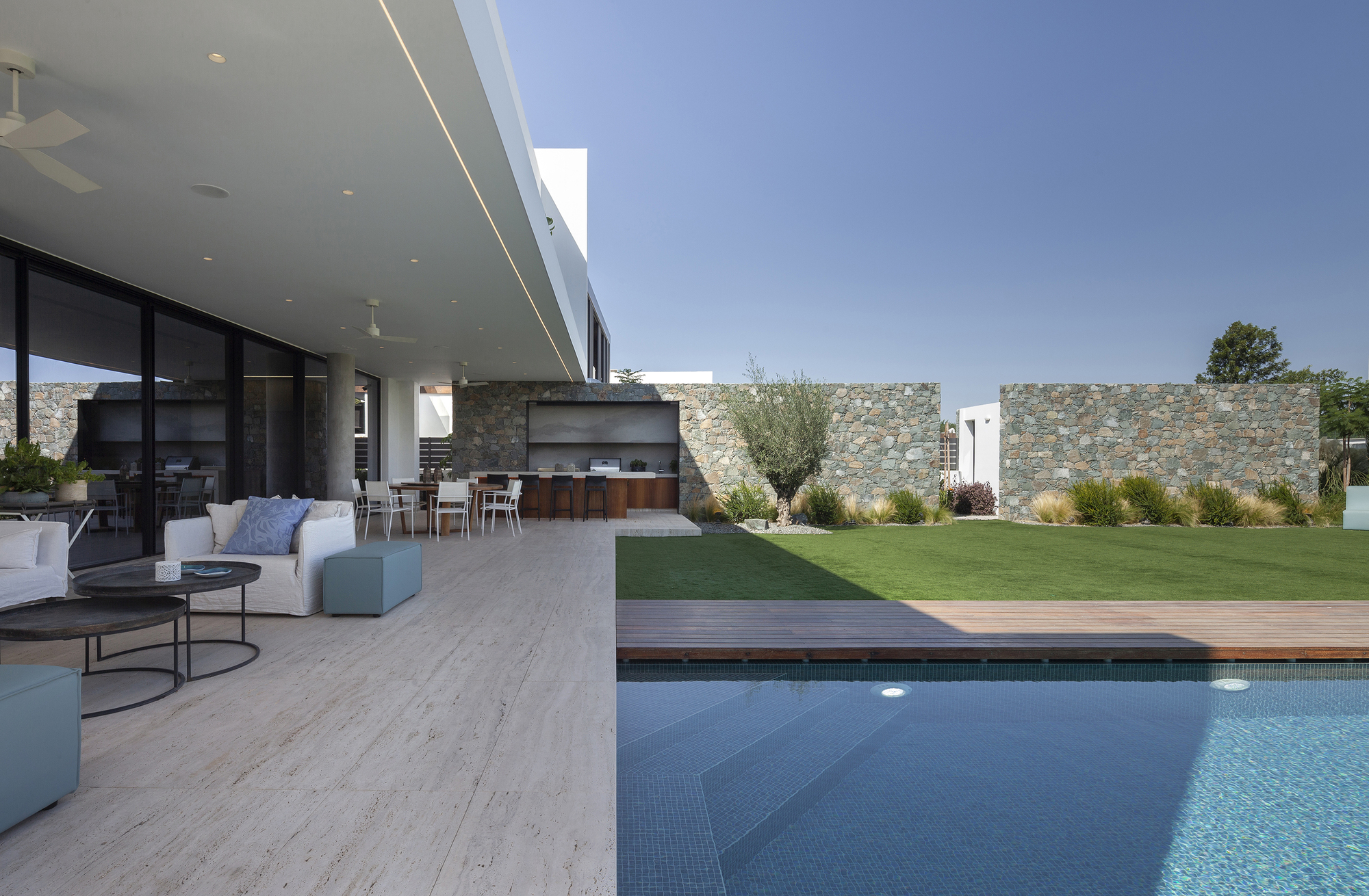 Covered terrace with travertine paving extending from the living area toward the pool and stone boundary wall