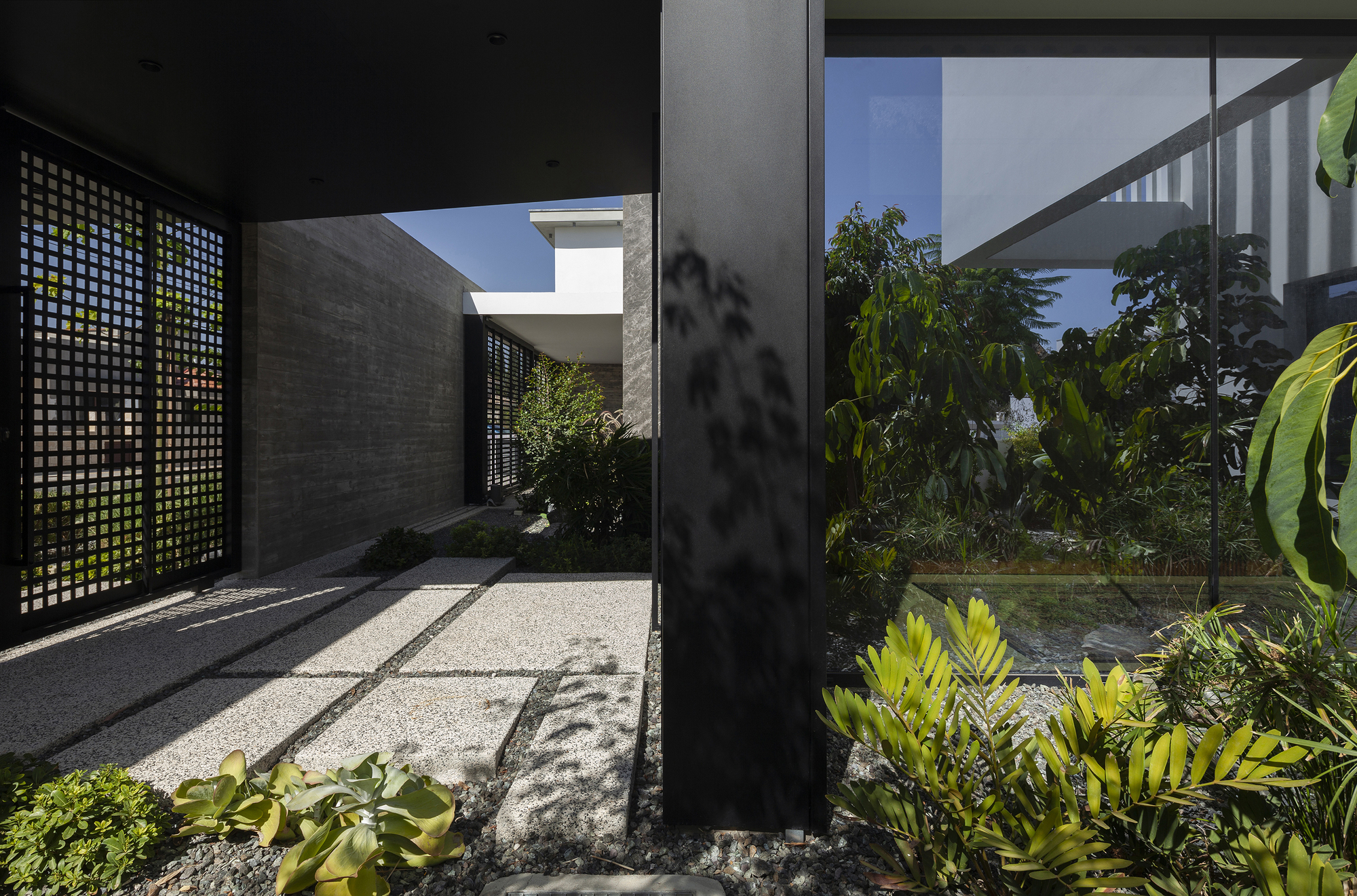 Lattice screen panel filtering dappled sunlight onto a gravel path with tropical planting along the walkway