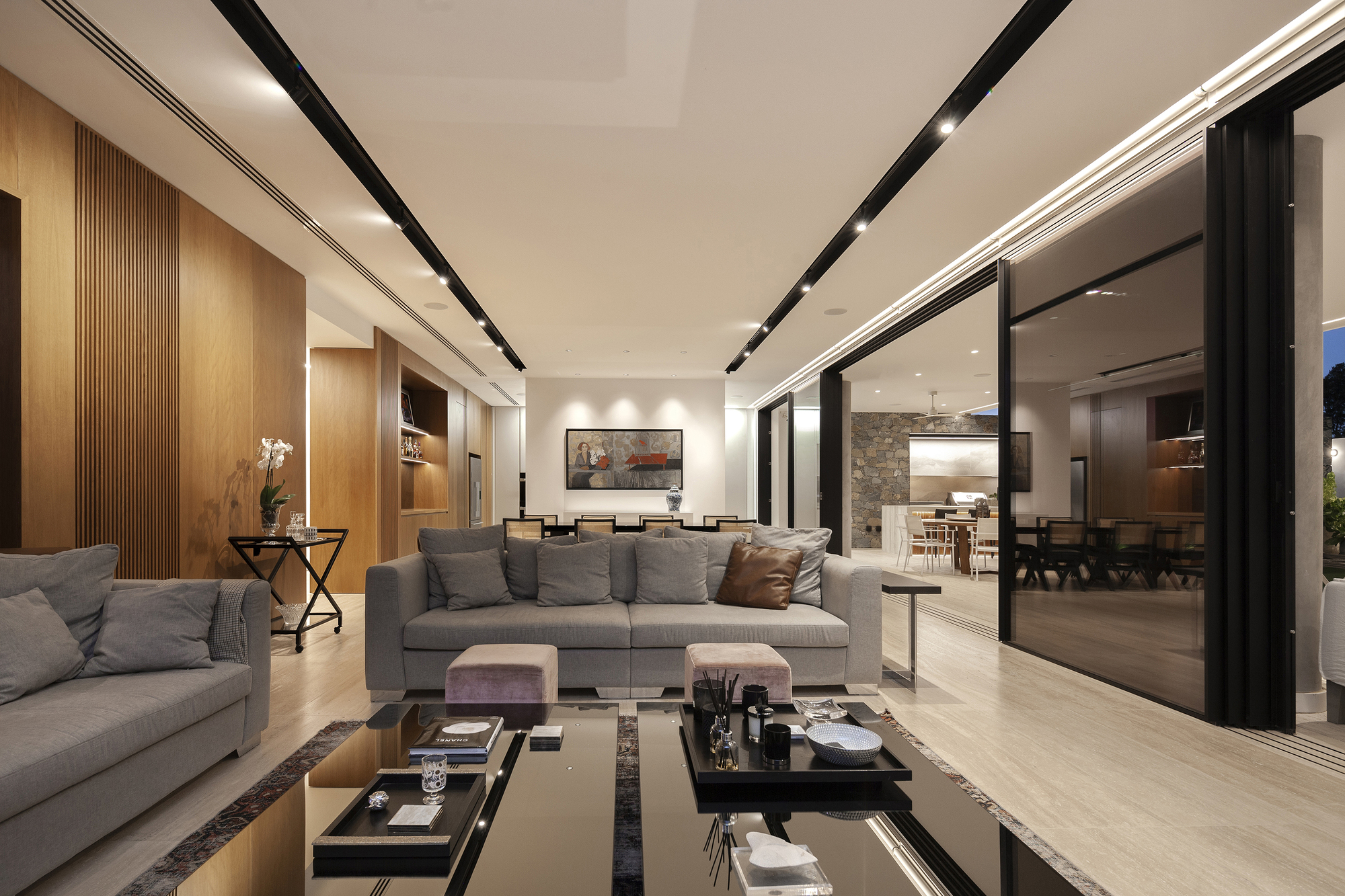 Open-plan living room with floor-to-ceiling glazing opening to outdoor spaces and recessed ceiling lighting tracks